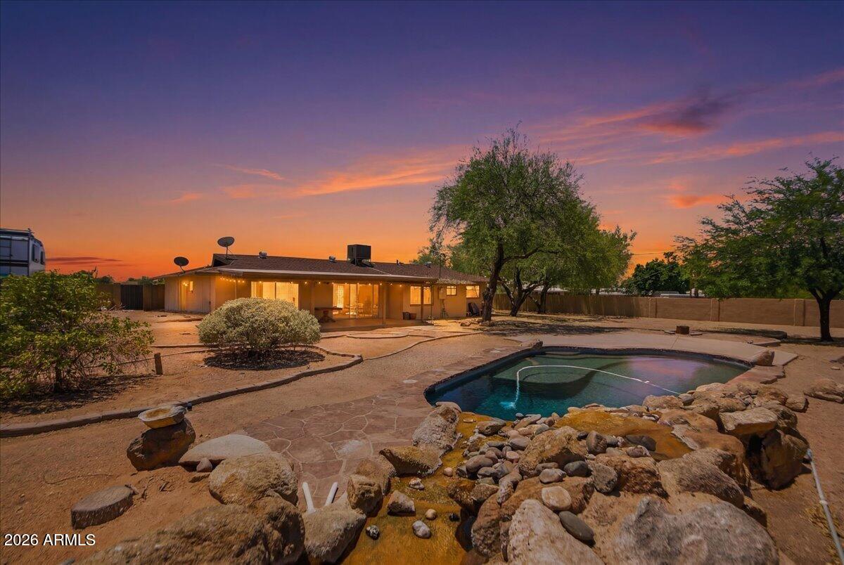 No HOA, over half an acre of land, for your trucks, trailers, or off-road toys. Tucked into a quiet pocket of Northeast Mesa, this property delivers the space and freedom that standard subdivisions can't touch. Sitting on a 21,000+ square foot lot, the exterior setup is designed specifically for outdoor enthusiasts, entrepreneurs, or anyone with a fleet of vehicles. The front features a clean circular driveway and a spacious two-car garage, while the side opens up to an oversized RV gate leading into a massive backyard. Whether you need dedicated parking for a toy hauler, utility trailers, or a blank slate to build out a custom workshop and event lawn, this yard handles it without a single neighborhood fine. Inside, the layout is highly functional, featuring a a distinct dual primary bedroom split floorplan and three full bathrooms. The living spaces and the main primary bedroom both feature oversized sliding glass doors, creating multiple direct access points to the back patio. The galley kitchen is equipped with granite countertops, a smooth top stove, and wall ovens, positioned right next to a large laundry room with extra storage capacity.
The outdoor living space centers around a pristine PebbleTec pool complete with a built-in water feature and expansive decking. The remaining land remains completely open, allowing the next owner to configure it to their exact specifications. Located just 10 minutes from the Salt River and minutes from the Loop 202, this home offers quick access to Saguaro Lake, hiking trails, A-rated Mesa schools, and upcoming commercial developments just down the road.