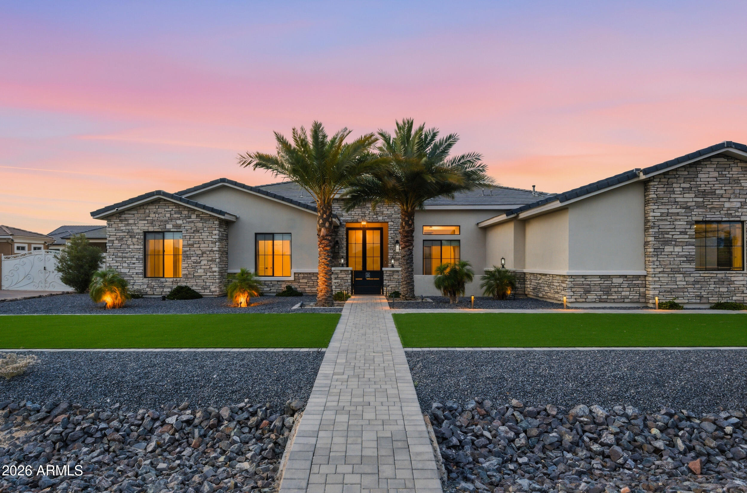 A striking custom estate in Russell Ranch, this 2021-built residence seamlessly blends refined design with effortless indoor-outdoor living. Set on an expansive nearly half acre lot with mountain views to the west, the home offers 3,873 square feet of thoughtfully curated living space, complemented by an RV garage--ideal for additional storage, recreational vehicles, or car enthusiasts.

Designed for both everyday comfort and elevated entertaining, the great room opens through pocket sliding doors to a resort-style backyard, complete with restaurant-grade misters, a fully integrated Sonos sound system spanning both interior and exterior spaces, and a covered outdoor living area anchored by a fireplace. Inside, a second fireplace adds warmth and ambiance to the great room. Just off the dining area, a temperature-controlled 250-bottle wine room adds a sophisticated touch, ideal for collectors and entertainers. The yard is prepped for a future pool, with infrastructure already in place.

At the heart of the home, the chef's kitchen features a statement Wolf range, dual Monogram dishwashers, oversized refrigerator and freezer, and a stunning quartzite island. A spacious walk-in pantry with a beautifully designed coffee bar, along with a beverage fridge and ice maker framed by bifold windows, further enhance the home's seamless indoor-outdoor flow.

The private owner's suite is a true retreat, offering a spa-like bath with steam shower, direct access to a well-appointed laundry room through the closet, and an adjacent flex space ideal for a Pilates studio or wellness room--complete with electrical ready for a sauna and windows on both sides for natural light.

Thoughtfully designed for comfort, the home features dual-zone HVAC systems providing independent climate control for each wing. The guest wing also includes a versatile bonus space, currently used as a playroom, easily adaptable as a media room or additional lounge. Custom window treatments are installed throughout, and the home is equipped with an integrated ADT security system with cameras and multiple access panels.

A rare opportunity to own a modern desert retreat where thoughtful design, comfort, and lifestyle come together in one of Litchfield Park's most sought-after communities.
