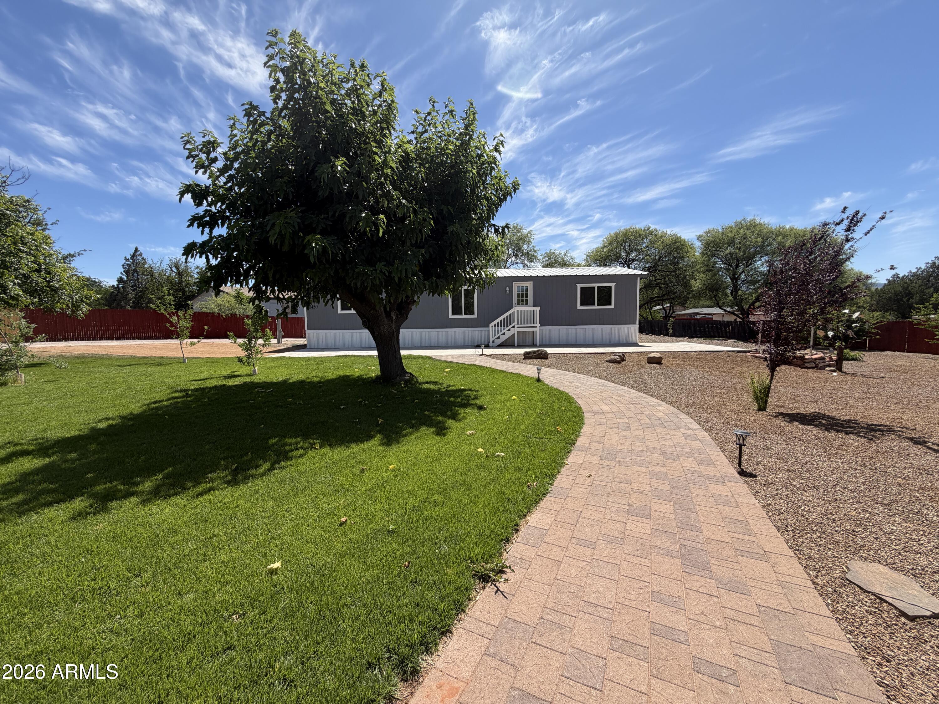 this 1568 sq.ft manufactured home offers three bedrooms and two bathrooms with updates throughout. Interior features include new flooring, updated countertops, fresh paint, new flooring, and real tile showers. Each room has mini splits for independent climate control. A tin roof adds durability and efficiency. Exterior highlights include stunning custom walking paths, wrought iron gates, grass, fruit trees, mature trees tying into desert landscaping throughout the property. The backyard includes a large paver patio, faux grass, more trees, and a garage or workshop. Property is turn key.