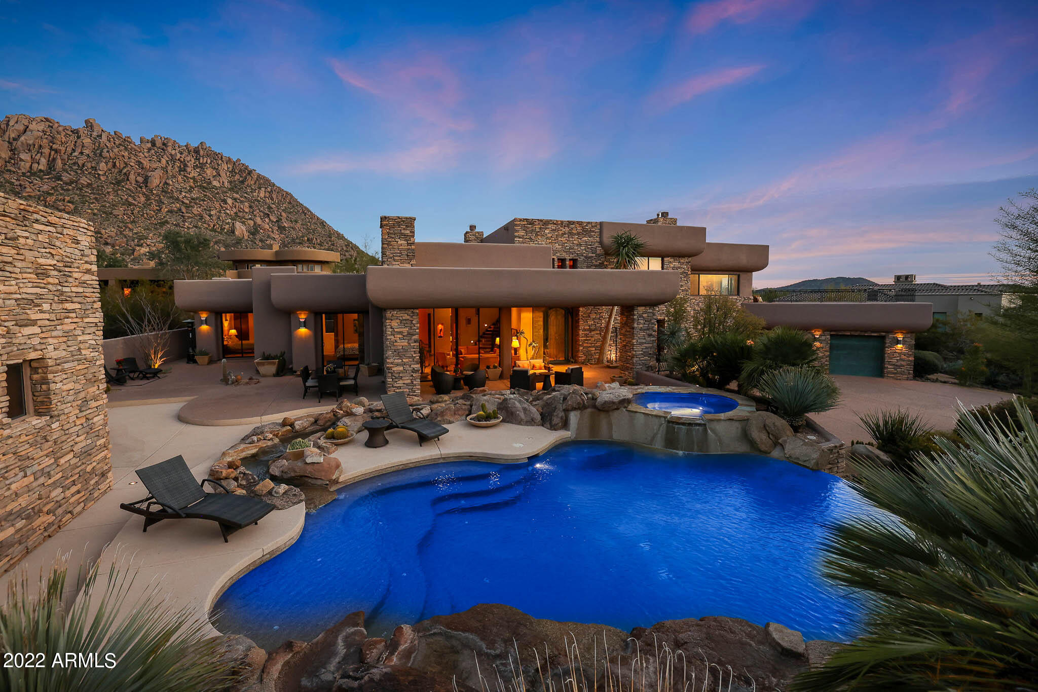 This unique desert contemporary house is located in the sought-after, guard-gated Windy Walk Estates in Troon Village. Situated on a generous and tastefully landscaped 3/4 acre lot, this 5,474 square foot home is set back from the street and has an impressive and timeless stacked-stone facade. The house has significant architectural interest with clean lines, high-ceilings, curved interior walls, and coffered ceilings with recessed lighting. Three interior fireplaces with black steel surrounds/clay accents and multiple art niches add charm to this home designed to maximize spectacular Pinnacle Peak views with Troon Mountain serving as a backdrop. The large living room floor-to-ceiling windows of butted glass take in dramatic Pinnacle Peak views & provide easy outdoor access. Bringing in lots of natural light. The entry foyer and living room have soaring ceilings and track lighting to provide a dramatic entry to the rest of the house. The impressive pool area has an elevated spa that cascades into the pool below with a flowing stream and a programmable boulder waterfall and negative edge. Multiple outdoor seating and dining area options are enhanced with a two-way, stacked stone gas fireplace and lush landscaping.

The kitchen and adjoining family room are designed for entertaining with an oversized kitchen island, 48" range (with grill and griddle), dining nook space, spacious pantry as well as an adjoining room for more formal dining. A wet bar with wine cooler separates the family and living rooms and provides easy access from both areas.

Spacious sitting/office area with wet bar, wine cooler and fireplace has striking Pinnacle Peak views and provides an inviting transition to the recently remodeled primary suite. With its own sitting area  and breathtaking mountain views through a twelve foot picture window. Frosted architectural glass doors lead into the spa-like primary bath with a steam shower, jet tub, solar-tube skylights and very spacious his and her walk-in closets. The terrace off of the primary bedroom has a sitting area to take in sunsets views over Pinnacle Peak as well as city light views.

Two additional en-suite guest bedrooms with spacious walk-in closets have direct access to the patio and mountain views through sliding doors. A large detached stacked stone Casita compliments the main house and has a breakfast bar with built-in microwave and beverage fridge. Sliding doors provide views from the Casita to the pool area and waterfall. The oversized 3-car garage has a generous storage room with built-in shelving. A multi-zone security system and five zone AC units provide flexibility and energy efficiency. 

This exceptional location is within walking distance to Troon Country Club and just minutes away from Pinnacle Peak, Brown's Ranch and Granite Mountain hiking trails and the Four Seasons Resort. Most furnishings and accessories are available by separate bill of sale.