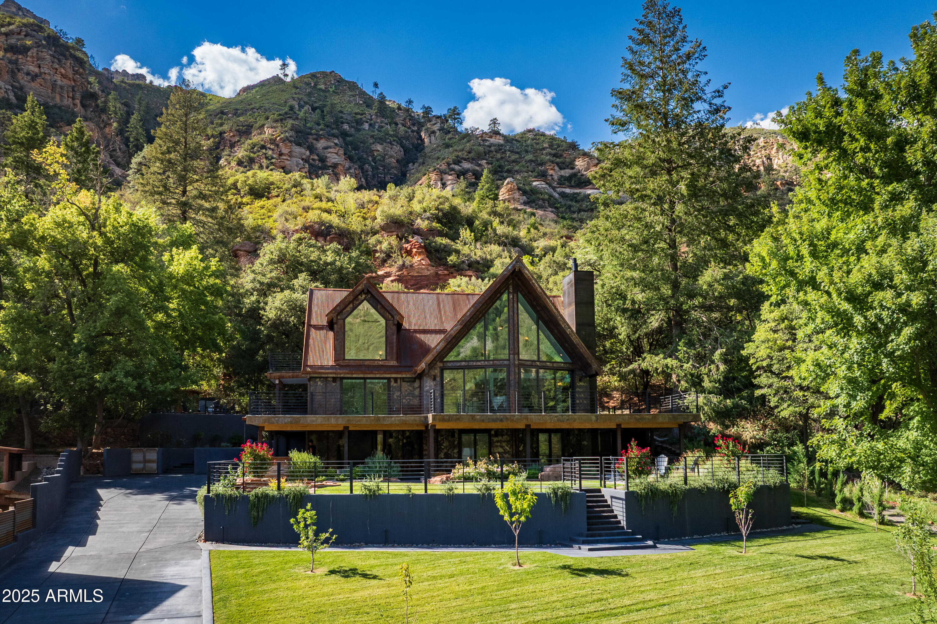 Mountain Modern Getaway. Step into a world where luxury meets serenity at this fully reimagined 2024 Mountain Modern masterpiece, tucked within the gated, creekside enclave of Junipine Estates, one of Oak Creek Canyon's most cherished communities. This rare 5 bedroom, 4.5 bath sanctuary backs to National Forest land and captures breathtaking views of the towering canyon walls that shift with the light throughout the day. Junipine Estates is more than a neighborhood, it is a living piece of history, offering 10 acres of lush common grounds along Oak Creek, a heritage apple orchard from the 1800s, a historic water channel, and a shared interest in the Purtyman Cabin, a Sedona landmark dating to the 1880s. Clad in striking Corten steel siding, the home blends strength, durability, and style. Inside, 22 foot ceilings and walls of glass frame the surrounding fir, pine, and juniper trees, immersing you in nature while the sounds of the creek provide a constant, soothing backdrop.

Two spacious primary suites, each with a Juliette balcony, include a spa-like steam shower for the ultimate retreat.

Designed for seamless indoor and outdoor living, disappearing sliding glass walls invite cool canyon breezes and dissolve the boundary between home and nature. Nearly 1,000 feet higher than Sedona, the climate is refreshingly cool in summer with crisp autumn evenings perfect for fireside gatherings.

Expansive wraparound decks create endless options for starlit dining, morning coffee, or simply taking in the canyon's beauty.

The gourmet kitchen opens to an al fresco dining area, while the grounds offer a lush front lawn with pear trees, a terraced garden with firepit and red rock water fountain, and a back patio where the historic water channel flows gently past.

End each day in pure relaxation as you enjoy the infrared sauna, gather with friends around the firepit, or soak in the eight person Jacuzzi under a brilliant canopy of stars.

This is more than a home, it is a rare opportunity to experience a storybook life in one of the most exclusive creek front neighborhoods in Oak Creek Canyon.