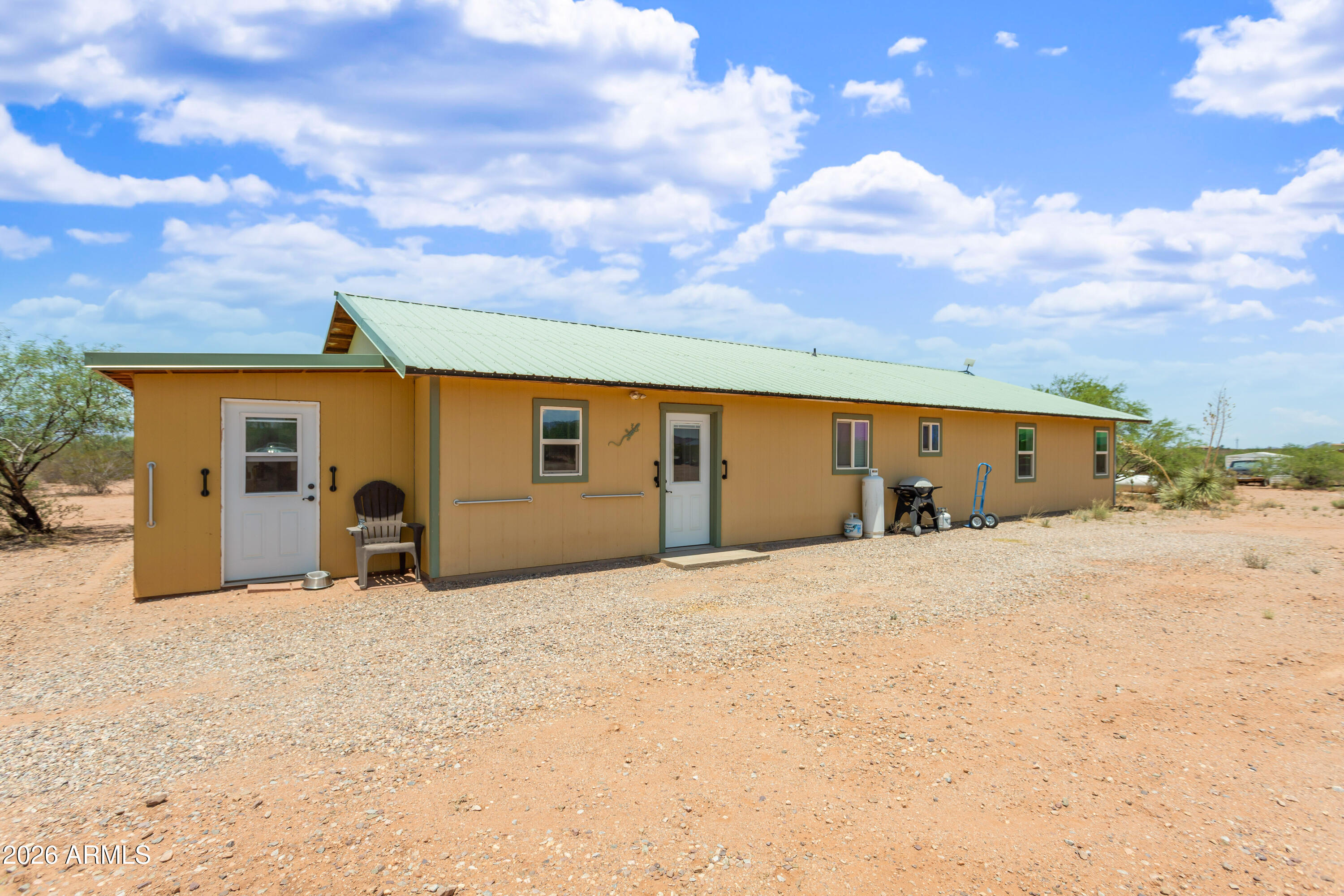 An automated gate invites you to this gently lived in home on over 13 fully fenced acres with stunning panoramic mountain views. 1 1/2 of the 4 sides is BLM land adding additional peace and privacy. In the kitchen you'll find nice counter tops, an electric range with double ovens, also a brand-new dishwasher & hood. Down the hall is a dedicated large laundry area with larger washer / dryer units, this room can double as a workspace or host a small gym. Common areas host LVP flooring while carpet in the bedrooms. 2 bedrooms have direct access to bathrooms, while the 3rd has two closets, all have a switch to control the hallway light for added convenience. On the property you'll find 2 sheds, a chicken coop, detached carport, also a workshop and well house with power The well house hosts additional laundry hook-ups and a window AC unit. Spigots are plentiful and there are a couple of Rv hook-ups. The home has a dedicated yard for pets and the parcel is also partitioned into two larger chunks that can connect via two gates on each end. The home is on slab, has a metal roof, and is supplied by a private well. Whether you're a hobbyist, enjoy toys or animals, or just want to be in a newer rural property with city access in minutes this is for you!