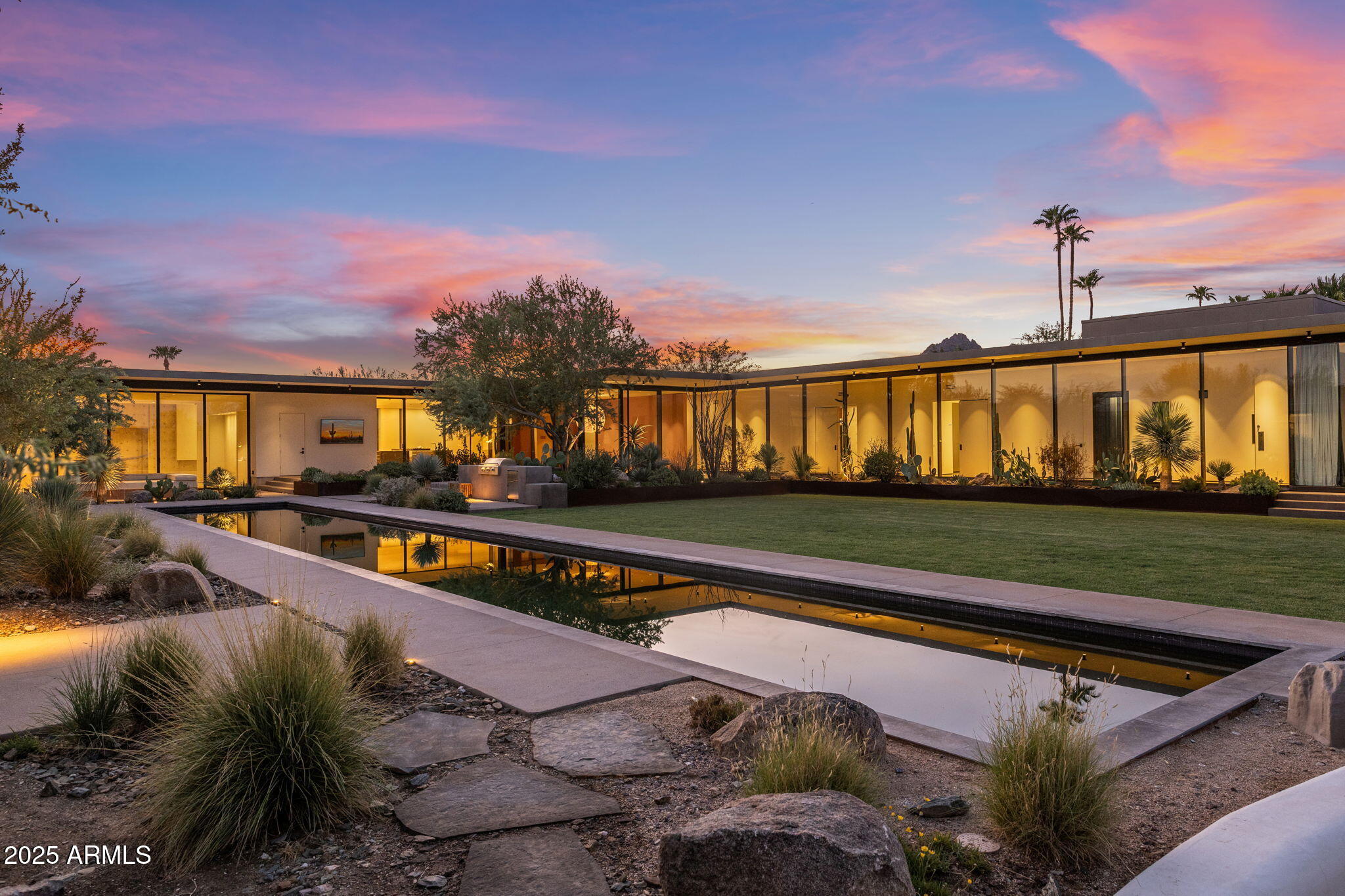 One-of-a-kind Modern Desert Contemporary Estate set on a private 1.72-acre corner lot with unobstructed views of Camelback Mountain, the Praying Monk, and Piestewa Peak. This private architectural masterpiece spans 10,865 sqft and was crafted with the highest level of design and materials. Built in an angled ''U'' shape, the residence showcases poured-in-place concrete, custom pivot doors, and expansive floor-to-ceiling glass walls that capture dramatic desert light while framing the mountain views and vibrant landscaping. Two mirrored corridors balance the design: one dedicated to the primary suite with an additional ensuite study/guest bedroom, the other to a theater, two ensuite bedrooms, and a versatile gym/flex space complete with steam shower and sauna. At the heart of the home, a voluminous living room with a double-sided fireplace opens to an adjacent lounge and bar, creating an ideal setting for both entertaining and displaying art that is enhanced by custom gallery-style lighting throughout. The expansive Bulthaup kitchen features a double island layout, Miele and Thermador appliances, generous storage, and a seamless connection to the family room with a custom media wall and breakfast area. A separate prep kitchen and butler's pantry complete the culinary experience. The formal dining room opens to the backyard with stunning views, blending indoor and outdoor living. The primary suite is a private retreat, distinguished by custom walnut cabinetry, a hidden wet bar, and two oversized walk-in closets. The luxurious bath features a Calacatta marble dual vanity with integrated storage, dual water closets, an oversized shower with dual showerheads, and a freestanding soaking tub overlooking a serene private courtyard that floods the space with natural light. The outdoor spaces are designed for both relaxation and entertaining, offering multiple gathering areas, a bbq area, seating lounge, grassy play pad, and a lap pool. Car enthusiasts will appreciate the 2,000-sq-ft double-height garage with three oversized bays,space for abundant cabinetry/storage, and direct access to the main residence. For larger collections, additional bays may be added on the adjacent land. A residence of this caliber must be experienced in person to truly appreciate its architecture, lifestyle, and one-of-a-kind presence in Paradise Valley.