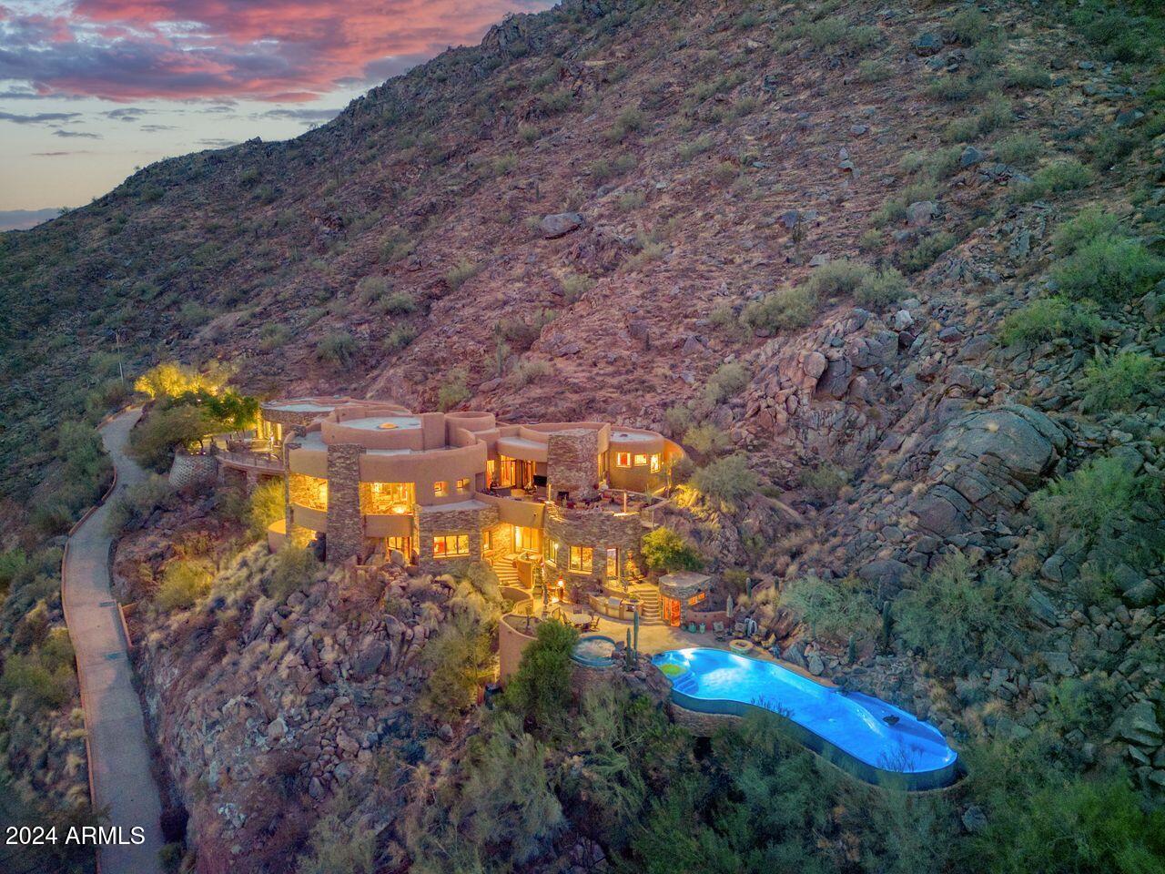 On 4 acres, majestically nestled on the highest point of Camelback Mountain. Designed by renowned architect Ken Hutchinson, the house is a sculpted piece of art, with walls following radius points of soft curvatures, some with a flowing ribbon effect. Eyes are drawn to an intricate, voluminous domed ceiling with groin vaults and an expansive 40-ft. radius wall of glass with unobstructed views towards the McDowell and Four Peaks Mountains and sparkling city lights. Boulder outcroppings have been thoughtfully incorporated into the architectural design, creating a striking visual statement. A cantilevered, 52-ft. mosaic-tiled pool and spa, an outdoor kitchen and sauna are the destination point for an unparalleled luxurious outdoor lifestyle. The split primary bedroom features a private upper upper deck view patio with an entertainment center and another fireplace, dual baths and highly finished walk-in closets. Guest bedrooms enjoy a secondary family room opening to a view patio. This sculpted piece of art offers a truly remarkable living experience. Only the 2nd offering of this precious, iconic property, at the zenith of Camelback Mountain.