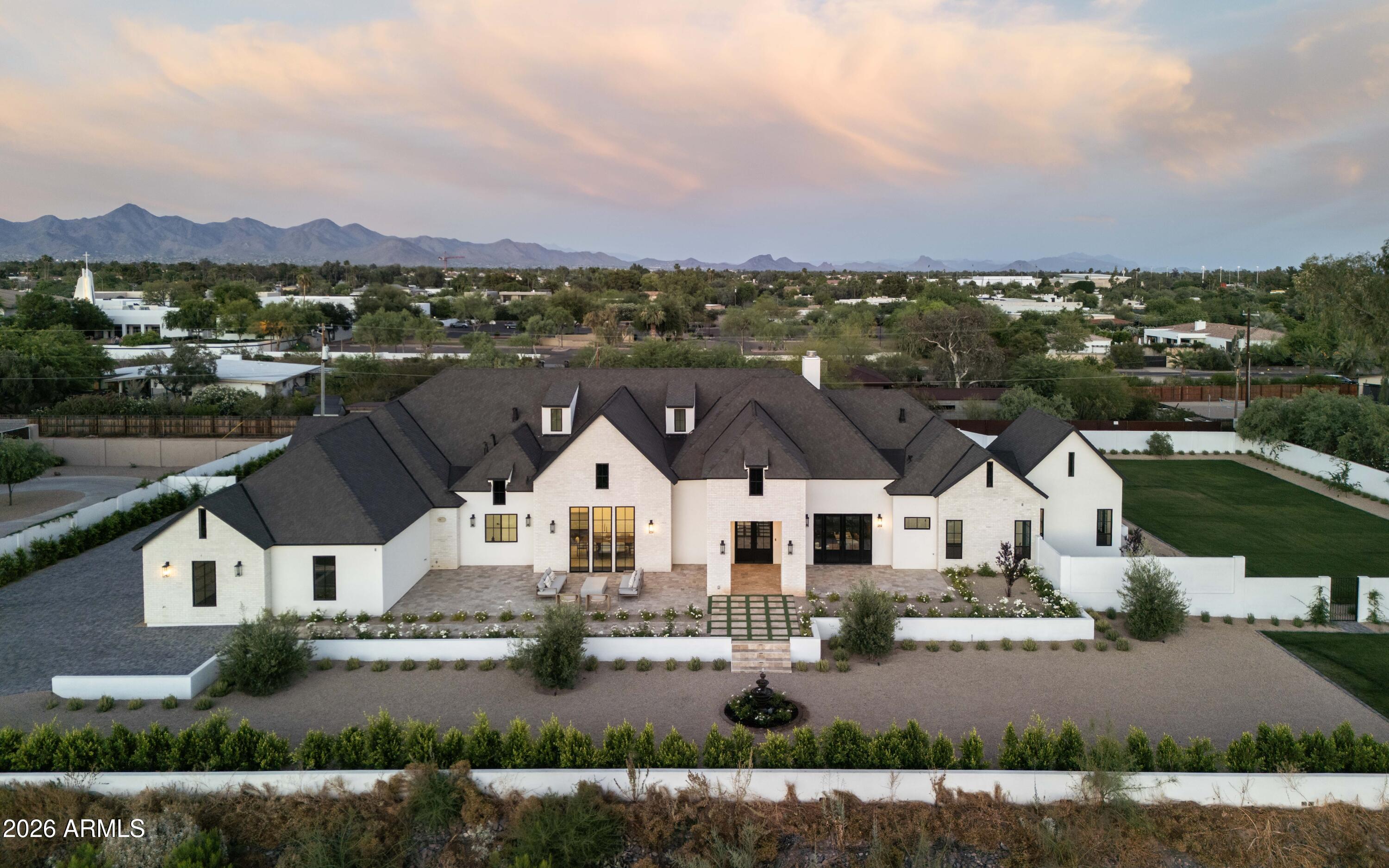 Anchored by classic French château architecture and reinterpreted through a modern lens, this new construction Paradise Valley estate spans nearly 6,000 square feet on a rare 1.045-acre parcel. A thoughtfully executed split floor plan offers five ensuite bedrooms, a private office, powder room, and a flexible secondary space suitable for a gym, theater, or studio. Soaring vaulted ceilings and clean architectural lines define the interiors, while a chef's kitchen outfitted with Wolf and Sub-Zero appliances serves as the heart of the home. The primary suite is a private retreat, featuring a fireplace, spa-inspired bath with freestanding tub, and direct access to outdoor living; designed with a sparkling pool, built-in barbecue, firepit, and generous open space. ADDITIONAL FEATURES AND UPGRADES 

All ensuite bedrooms with private patio access and direct backyard entry
Dedicated office with dual exterior access to front courtyard and patio
Grand great room with 18.5-ft vaulted ceilings, four dormers, and statement fireplace
Formal dining room with vaulted ceiling
Flexible bonus space ideal for theater, gym, or game room
Fully retractable pocket doors for seamless indoor-outdoor living to pool and built-in BBQ
Chef's kitchen with 14' x 6.5' island, full slab quartz, Sub-Zero appliances, wine fridge, and walk-in pantry
Primary suite with vaulted ceilings, fireplace, and direct patio access
Spa-inspired primary bath with freestanding tub, oversized dual shower, dual vanities, and private water closet
Custom walk-in closets throughout
Wide-plank engineered hardwood flooring
Oversized 4-car garage
Expansive 1-acre lot with unobstructed mountain views; room for tennis, pickleball, or sport court
Newly built PebbleTec pool with Baja shelf and sun lounging deck
Travertine hardscape across all outdoor living areas
Lush grass lawns in both front and backyard
Brand new septic system
Built-in fire sprinkler system
Electric vehicle charging capability
Fully wired for security system, Wi-Fi, and whole-home TV integration with exterior cameras