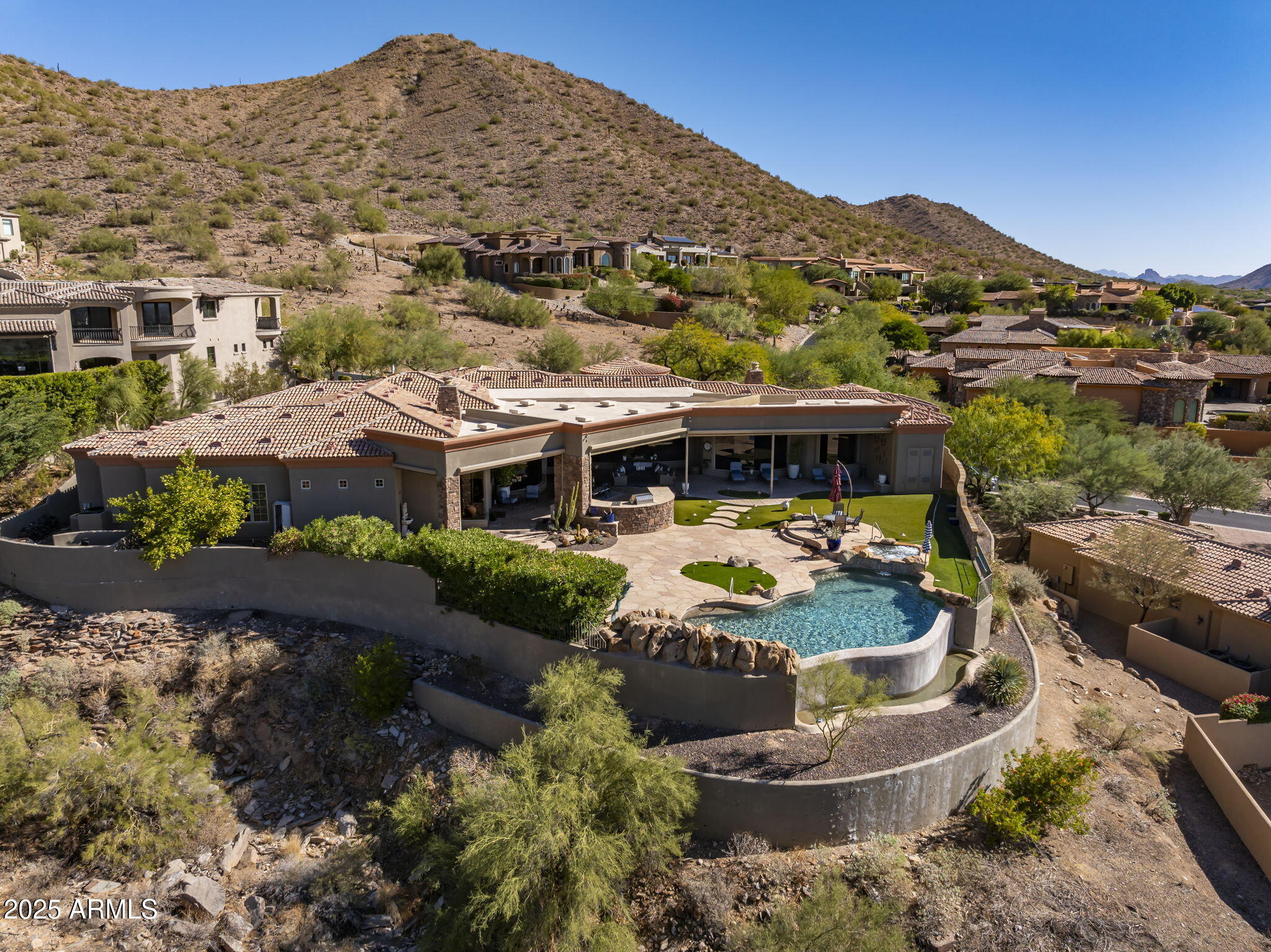 Situated on one of the highest lots in Ancala, this exquisite home is listed at its recent appraised value and boasts a meticulously crafted layout with designer decor throughout. The grand iron entry doors open to reveal an impressive 20' wide x 11' high wall of glass providing uninterrupted panoramic views of Camelback Mountain over a negative-edge pool with stunning rock waterfall. The breathtaking scenery stretches for miles, creating a truly one-of-a-kind backdrop. This view follows you from room to room as the entire south-western surface of the home is dominated by this uninterrupted solid Pella glass. Perched high above the Valley, any harsh west-facing exposures are softened by expansive overhangs without affecting these dramatic views. There are no steps anywhere in the home. As