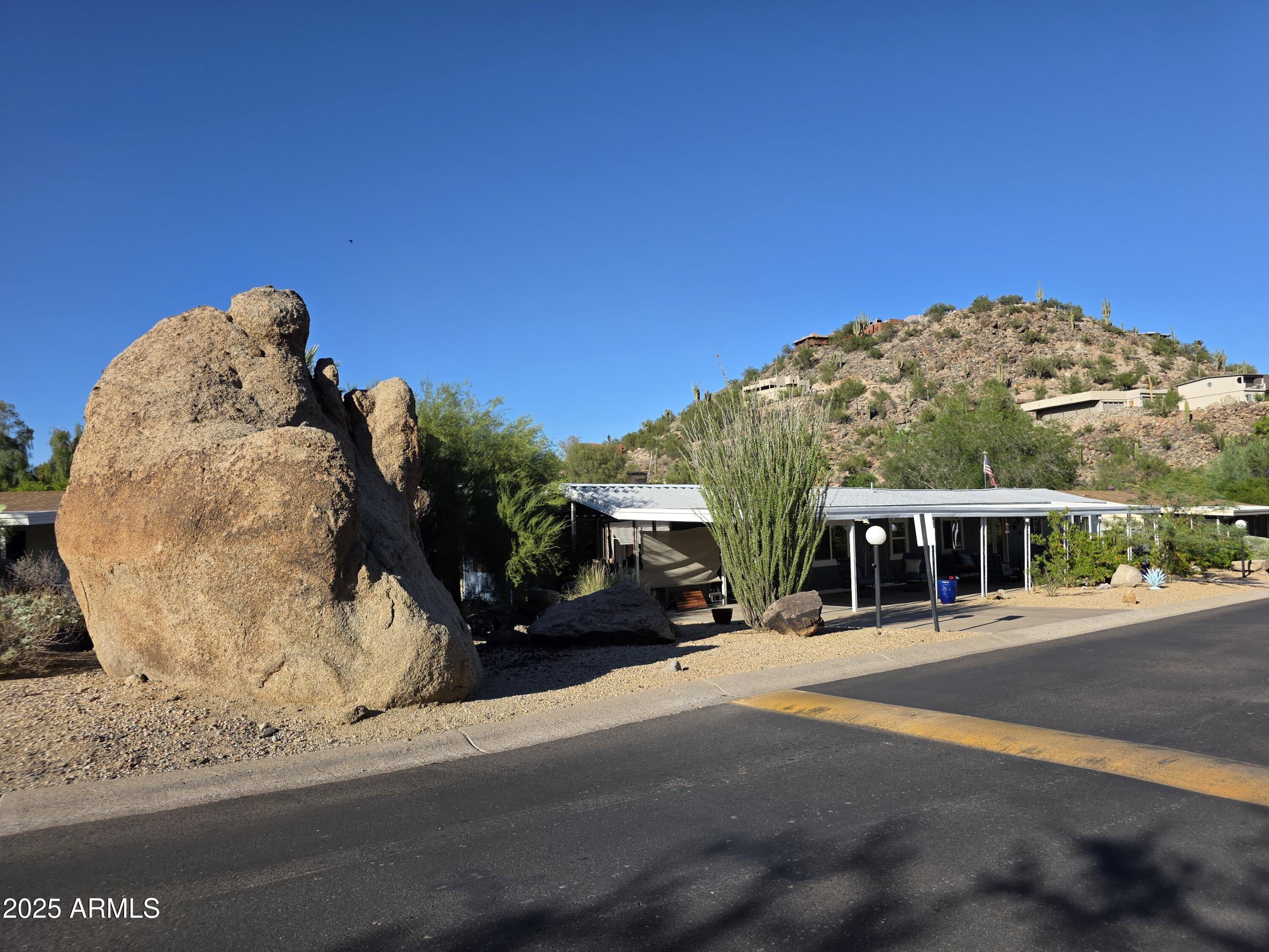 Oversized 70'x16' (1,120 sf) single-wide with great views of the boulders! Desirable split 2 bed, 2 bath floor plan with new roof (2024),  exterior paint (Sept 2025). Features vaulted ceilings, double-pane windows, ceiling fans, and a spacious kitchen with granite counters, breakfast bar, island, hallway pantry, and heavy-duty metal pull-out drawers. Stainless steel appliances, two refrigerators, washer, and dryer included. Great room layout ideal for entertaining. Oversized covered patio with double-door entry & extra-long carport for up to four cars. Community offers 2 pools, pickleball, tennis, clubhouse, and more. No rentals allowed. Park requires minimum credit score of 750, 3x the lot rent in verifiable monthly income, & pass a background check. 55+ Community. Lot Rent $1030 monthly