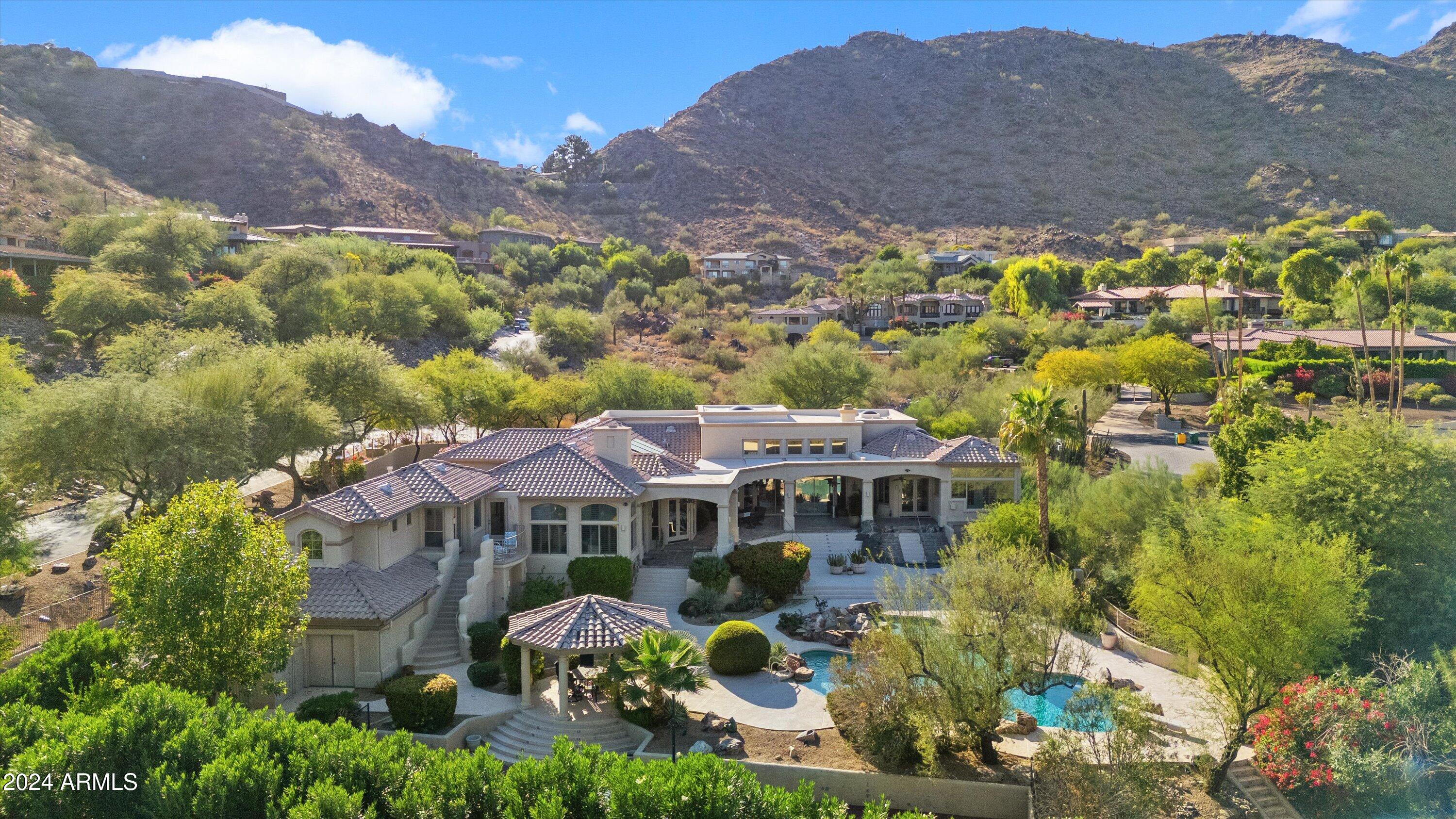 Nestled in the desirable Tatum Canyon of Paradise Valley, this exceptional home spans over 6,174 square feet on a private acre corner lot, offering sweeping mountain views in every direction. Designed for sophisticated living, this residence blends elegance with practicality.On 
 entering, one is greeted by a light-filled great room with soaring ceilings, glass walls, and sliding doors that create a seamless flow between the indoor and outdoor spaces. A meticulously landscaped backyard offers the ultimate retreat with a stunning pool, water
features, spa, outdoor BBQ, ramada, a sport court ideal for pickleball, and beautiful lawns —
all set against the backdrop of the canyon's natural beauty. The home boasts four spacious bedrooms, a dedicated office The primary suite, positioned in its own wing, is a luxurious sanctuary with a lavish bath, a 360-degree mirrored dressing room, and a cozy sitting area complete with fireplace.
Designed with entertaining in mind, the chef's kitchen is a culinary masterpiece, equipped with Viking appliances, concrete countertops, and a professional-grade wine cellar. An 8-foot butcher-block island, floor-to-ceiling stone fireplace, and open-concept design make the kitchen and family room perfect for both intimate and grand gatherings. Additional spaces include a formal dining room with a dry bar, family room, and a 25-foot game room with a wet bar. Each of the four bedrooms is en-suite, with a guest suite for ultimate privacy. An elegant living room along with a library/office with a loft, complement the living areas.
Previously owned by a sports star's family, this one-of-a-kind home offers an unparalleled opportunity to own a private, gated resort with dramatic views, luxurious amenities, and the perfect blend of comfort and elegance. Conveniently located with easy access to premier shopping, dining, hiking, and biking trails, this
home is just a short drive from Phoenix Sky Harbor and Scottsdale airports, making it the ideal combination of luxury and convenience.