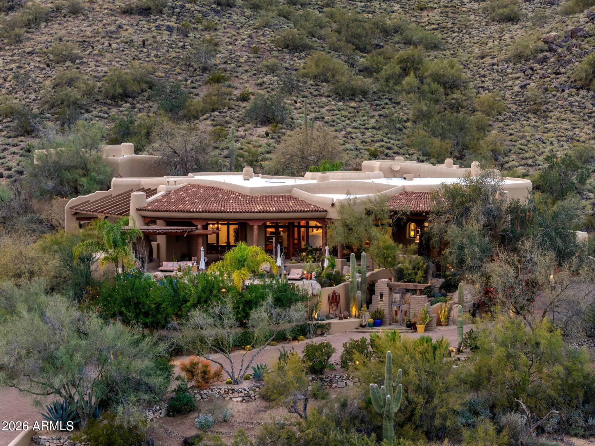 This beautifully decorated and thoughtfully remodeled organic Pueblo style estate is a must see in person, with incredible views that truly have to be experienced to be believed. Set high on Lone Mountain in the guard gated community of Sincuidados, the property spans 3.4 acres across double lots, with an additional adjacent acre offering the possibility for the future expansion. Perched on an exceptional view lot, the home captures magnificent mountain and city light views from virtually every room, delivering extraordinary privacy while still enjoying the benefits of an active neighborhood.  Designed by award winning architect and Master of the Southwest Lee Hutchison, the residence showcases authentic Southwestern design with real hickory wood floors, polished concrete accents, substantial viga beams, and hand laid adobe brick walls. Handcrafted windows and screens and eight real gas fireplaces add warmth, character, and timeless appeal throughout. The spacious great room flows seamlessly into a gourmet kitchen featuring a Viking Professional 6 burner range, 24K gold farm sink, and hand painted tile accents. An elevator provides convenient access from the oversized four car garage, complete with new epoxy flooring, built in cabinetry, and a large storage room, directly to the main family room and kitchen level. The primary suite serves as a private retreat with a gas fireplace and spa like bath showcasing a jacuzzi soaking tub perfectly positioned to take in the mountain views, along with a custom steam shower. A detached casita offers its own private escape with sweeping city light views.Outdoors, a heated infinity edge pool with dark pebble finish and jetted spa appear to spill into the surrounding desert and distant mountains. Multiple covered flagstone patios and an outdoor kitchen with a Viking BBQ create ideal spaces for entertaining against a backdrop of dramatic desert scenery. The cost to replicate this home today, along with its magnificent lots, represents an extraordinary opportunity to own a true view estate in one of North Scottsdale's most vibrant guard gated communities. Beautifully remodeled and impeccably maintained, this is a rare offering combining expansive acreage, unmatched privacy, and incredible views that must be seen in person to fully appreciate, with the added potential to expand on the additional lot with a new garage, guest house, or private pickleball court.
