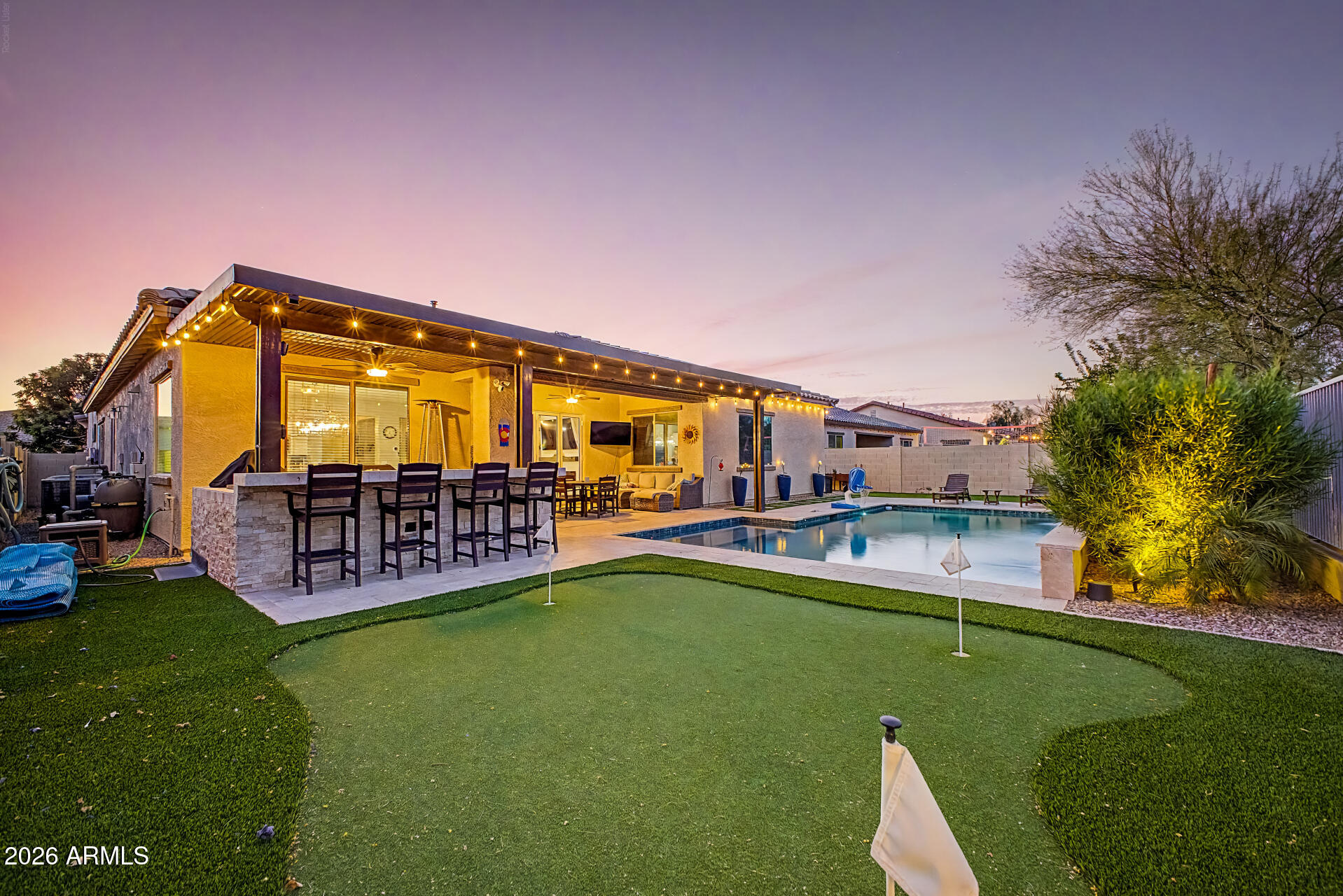 Discover luxury living in Palm Valley, one of Goodyear's most sought-after communities. This beautifully upgraded 4-bedroom, 3-bath home with a 3-car garage offers the perfect blend of style, comfort, and modern convenience. Recent upgrades include a stunning glass accordion wall for seamless indoor-outdoor living, a custom entertainment center with electric fireplace, and a flexible office space ideal for remote work or hobbies. Step outside to your private resort-style backyard featuring a sparkling smart pool with waterfall features and gas heat, low-maintenance turf, an extended covered patio, pergola, outdoor BBQ bar, and private putting green--perfect for entertaining and year-round Arizona living. Additional highlights include an EV charging station, wine fridge, reverse osmosis system, and smart home controls for the pool, lighting, security, and thermostat. Conveniently located near Loop 303, top-rated schools, premier shopping, dining, and championship golf courses, this move-in-ready Palm Valley home offers the best of luxury living in Goodyear, Arizona.