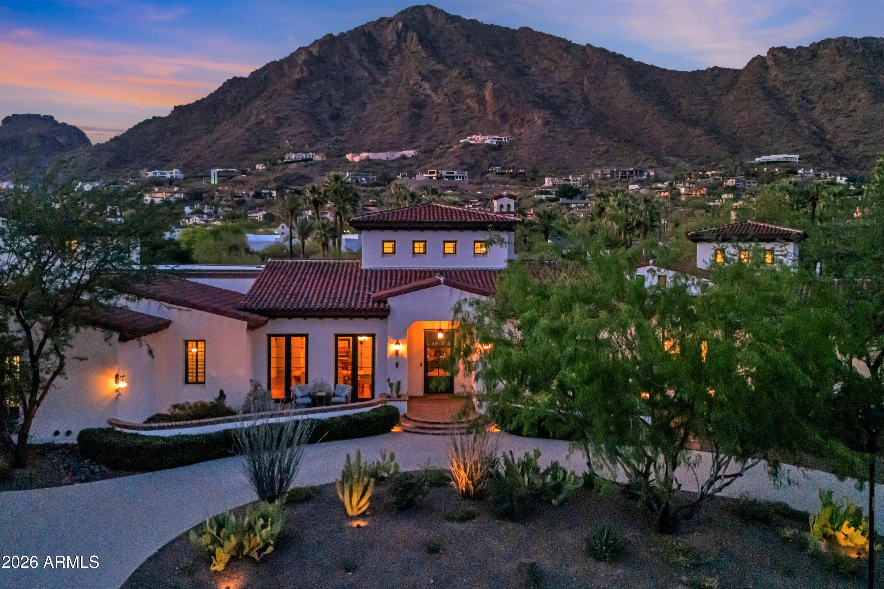 Set on over an acre at the base of Camelback Mountain, this Santa Barbara inspired estate is a rare expression of craftsmanship, scale, and design. Thoughtfully custom built with an emphasis on quality and detail, the home offers seamless indoor-outdoor living, expansive glass, and unobstructed mountain views that fill the interiors with natural light. Rich walnut flooring, custom millwork, and hand-crafted finishes define the living spaces, anchored by a chef's kitchen designed for elevated entertaining. The flexible floor plan includes multiple bedroom suites, a private guest retreat with separate living space, dedicated office and flex room with stunning views. Bathrooms feature artisan tile and refined natural stone, continuing the home's cohesive, high-end aesthetic. Designed for both comfort and performance, the home incorporates advanced climate control, automated systems, and superior construction quality. The grounds create a private desert sanctuary with a resort-style pool and mature, sculptural landscaping. A standout feature is the expansive climate controlled RV garage equipped with a large airplane hangar style door. It has space for 9 cars, along with a workshop ideal for enthusiasts.