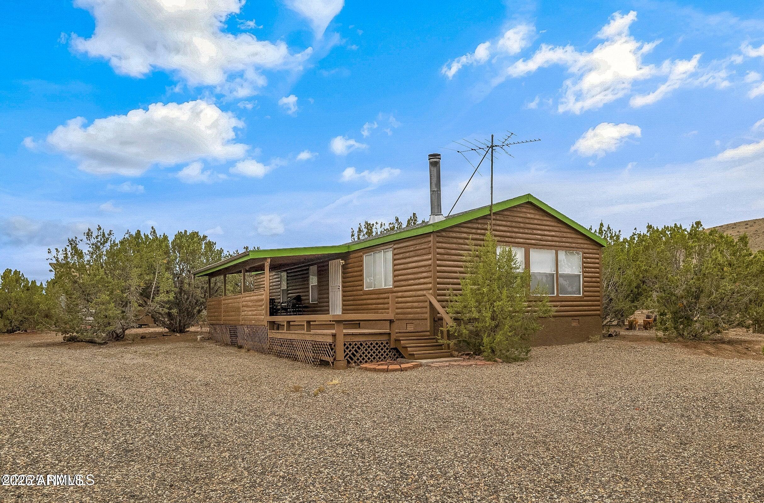 Escape the ordinary & embrace sustainable living on this beautifully treed 10-acre parcel. This 3-bed, 2-bath log-sided manufactured home offers 1,248 sq. ft. with new roofs installed in 2025, and a full solar + water system for off-grid independence. Step onto the expansive covered & open deck -perfect for morning coffee, sunset dinners, or stargazing under pristine night skies. Bonus structures include a 300 sq. ft. light-filled studio/office/game room with power & a separate powered storage space/workshop. Fully fenced with gated entry. Water delivery or nearby station options available. Whether you're seeking a peaceful getaway, a self-sufficient lifestyle, or a basecamp for outdoor adventure, this gem delivers freedom, functionality, and natural beauty in equal measures.