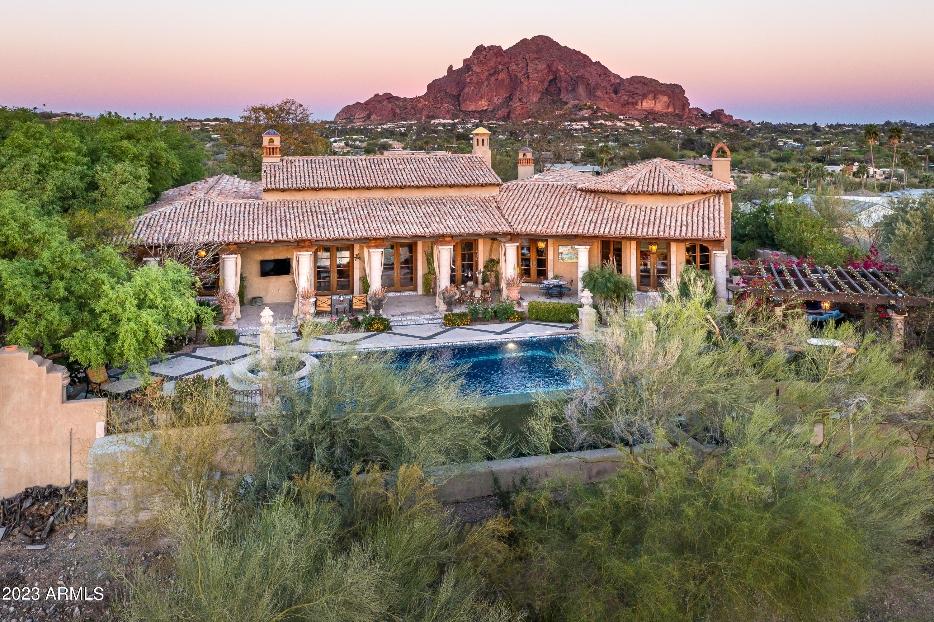 HUGE PRICE IMPROVEMENT**Nestled in the picturesque Paradise Valley, a Nance Construction built home stands as a testament to modern luxury and impeccable craftsmanship. With stunning 360-degree views that stretch as far as the eye can see, this architectural masterpiece offers an unparalleled living experience that seamlessly blends with its natural surroundings. As you approach the property, you are immediately captivated by its grandeur and beauty. A meticulously landscaped courtyard and circular drive welcomes you, adorned with vibrant flora and lush greenery that perfectly complement the surrounding desert landscape. The privately gated entrance leads you towards the magnificent entrance of the home and courtyard with authentic Iron doors and Mediterranean fountain.  (Continued Stepping through the front door, you are greeted by an open and inviting foyer that sets the tone for what lies ahead. The interior design exudes elegance, incorporating a blend of timeless touches and details of iron and rich woods. From the high ceilings adorned with intricate detailing to the custom-designed lighting fixtures, every aspect of this home is a reflection of refined taste and impeccable attention to detail. The expansive living spaces are designed to maximize both comfort and functionality. Arched windows and doors line the walls, allowing natural light to flood the rooms and offering breathtaking views of the surrounding valley and majestic mountains beyond. The open floor plan seamlessly connects the living room, dining area, and gourmet kitchen, creating a perfect space for entertaining guests or spending quality time with family. The kitchen is a chef's dream come true, equipped with top-of-the-line appliances, custom cabinetry, and a generous island for food preparation and casual dining. Stone countertops, sleek hardware, and designer finishes add a touch of sophistication to this culinary haven. Adjacent to the kitchen, a cozy breakfast nook with intimate brick fireplace overlooks the meticulously manicured backyard, providing a serene spot to enjoy your morning coffee while soaking in the beauty of the surroundings. The master suite is a sanctuary of tranquility, boasting a spacious layout and an abundance of natural light. The ensuite bathroom is a true oasis, featuring a luxurious soaking tub, a walk-in shower, and dual vanities. A private balcony extends from the master suite, offering a secluded retreat to enjoy the breathtaking sunsets or stargaze under the night sky. The additional bedrooms and guest suites are thoughtfully designed, each with their own ensuite bathrooms and ample closet space. These rooms provide a haven of comfort and privacy for family members or guests, ensuring everyone feels at home. The outdoor living spaces are equally as impressive as the interior. Expansive patios, strategically placed to capture the best views, provide the perfect backdrop for al fresco dining, lounging by the pool, or simply basking in the warm Arizona sun. The infinity-edge pool seems to seamlessly blend with the horizon, creating a serene oasis that invites you to relax and unwind and enjoy the mountain views or city lights. Beyond the pool, a meticulously landscaped backyard extends into the vast desert landscape, seamlessly blending the man-made and natural elements. Native plants, carefully selected tin the desert environment, adorn the property, creating a sustainable and low-maintenance oasis. In summary, a Nance Construction built home in Paradise Valley represents the epitome of luxury living. From its commanding presence to its thoughtfully designed interior spaces and captivating outdoor areas, this home offers an unparalleled living experience. With stunning 360-degree views, impeccable craftsmanship, and a harmonious integration with its natural surroundings, this architectural masterpiece truly embodies the essence of paradise.