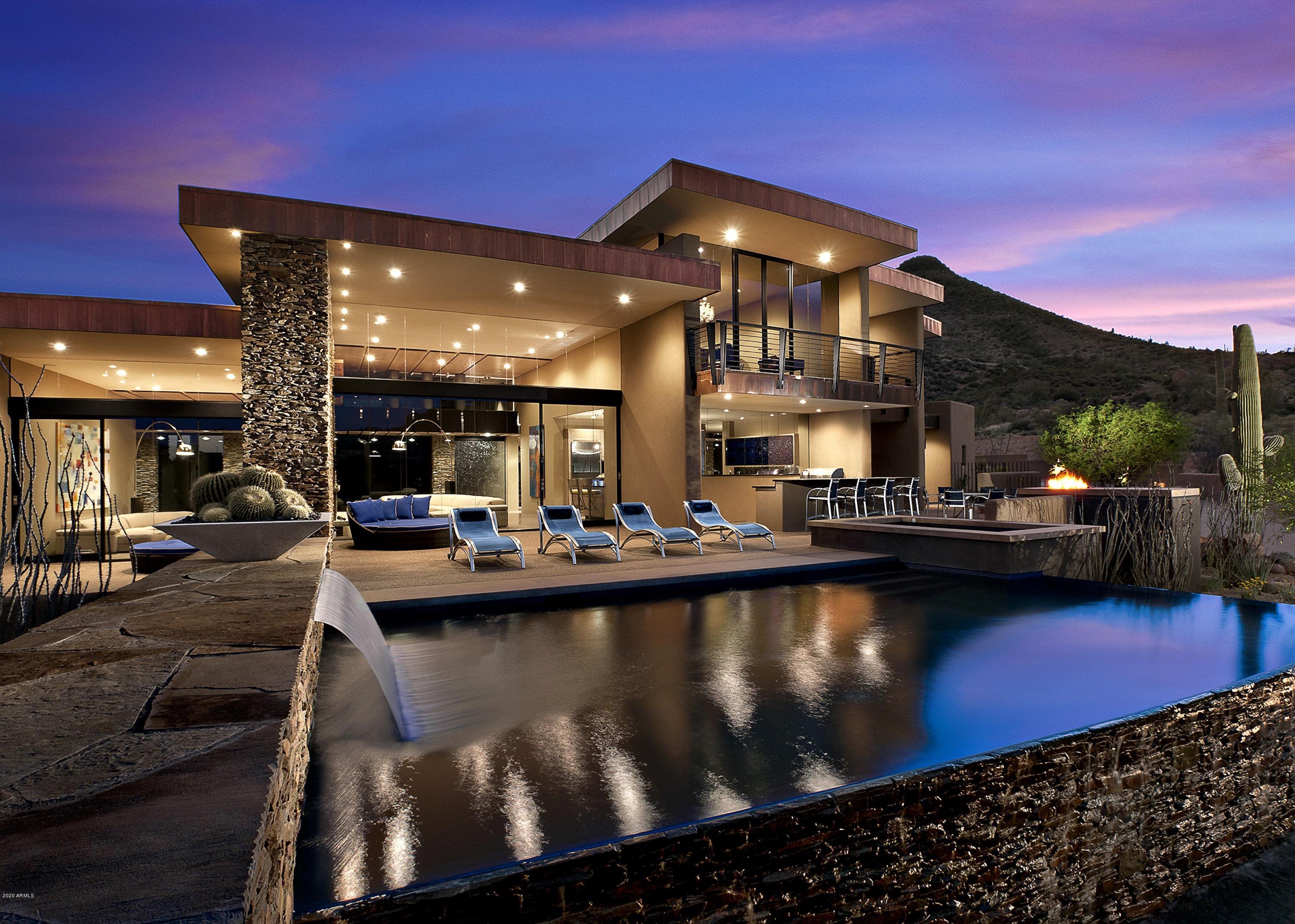 Custom Contemporary home on 5+ private acres. Pool orientation is North/ East with panoramic Mtn views. Architectural features: floating roofs & curvilinear elements, treated copper fascias, walls of glass and polished aggregate floors. The open plan main level includes living, dining,kitchen and hearth rooms, office, expansive master retreat w/ 2 massive  bath & closets, junior master and resort patio. Dramatic floating glass staircase leads to upper-level game room, additional guest quarters and a sunset & city light view-balcony. Exterior amenities include 5 fire features, 3 water features, family-sized pool, 2 spas. Conveniently located in Lone Mt. Village(additional access thru Carefree Ranch gates). 
The interior model train system is personal property and does not convey.