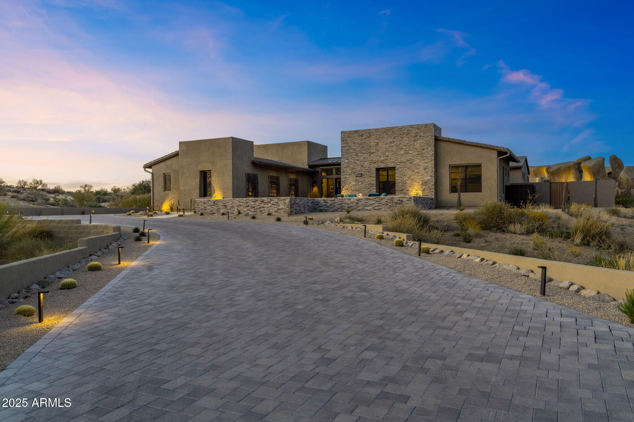 Experience unparalleled luxury living in Sereno Canyon with this extraordinary Toll Brothers estate, offered at ~$900,000 below replacement cost. Situated on a premium, boulder-framed lot, this highly upgraded home is a rare opportunity to enjoy refined elegance with breathtaking natural beauty. The streetscape features a massive paver driveway climbing through pristine natural desert to a groomed desert prelude. A limestone path leads you into the stacked stone front courtyard, where lush turf is accented by hibiscus, jasmine, lavender, and boxwood to create a serene oasis.  Enter through the iron front door where the grand foyer draws your gaze to the central courtyard and the stunning backyard beyond. The expansive great room is a masterpiece of design, anchored by an oversized horizontal gas fireplace swathed in agate-inspired tile. The custom kitchen is equipped with top-tier Wolf, SubZero, and Asko appliances, complemented by a double-waterfall island wrapped in natural quartzite that continues on the counters and backsplash. For work or relaxation, the office pampers with double-door entry, views of boulder formations both in and out of the yard, and a striking soft-touch designer wall treatment. The primary suite is a sanctuary featuring the owners' private media room and an oversized bedroom, both with custom wood slat wall treatments. The opulent primary bath showcases tasteful tile and granite finishes, with back-lit floating mirrors. The guest wing offers a luxurious powder room, plus three additional bedrooms, each with its own custom bath en suite. Wine enthusiasts will appreciate the 102-bottle SubZero wine fridge paired with a custom wine-cork countertop and ample storage for stemware and libations. The five-car garage boasts epoxy flooring, extensive storage solutions, and a custom workbench with tool drawers. Step outside through custom 20' corner glass doors to discover your private paradise. The backyard features lush landscaping, a never-used grill station, and a dramatic 28' reverse negative edge waterfall cascading over iridescent glass tiles framed by stacked stone planters. The elevated spa is wrapped in matching glass tiles and spills over to the pool's baja shelf. Enjoy leisure time on the 4-hole putting green or gather around the granite-slab firepit and banco nestled into towering natural boulders.  The central courtyard offers more surprises--covered and open patios share a two-way fireplace, while a lush side yard rivaling most backyards, is crowned with another custom banco with sweeping views of Tom's Thumb and the McDowell Mountains. We urge you to compare to new!  This home has it all!