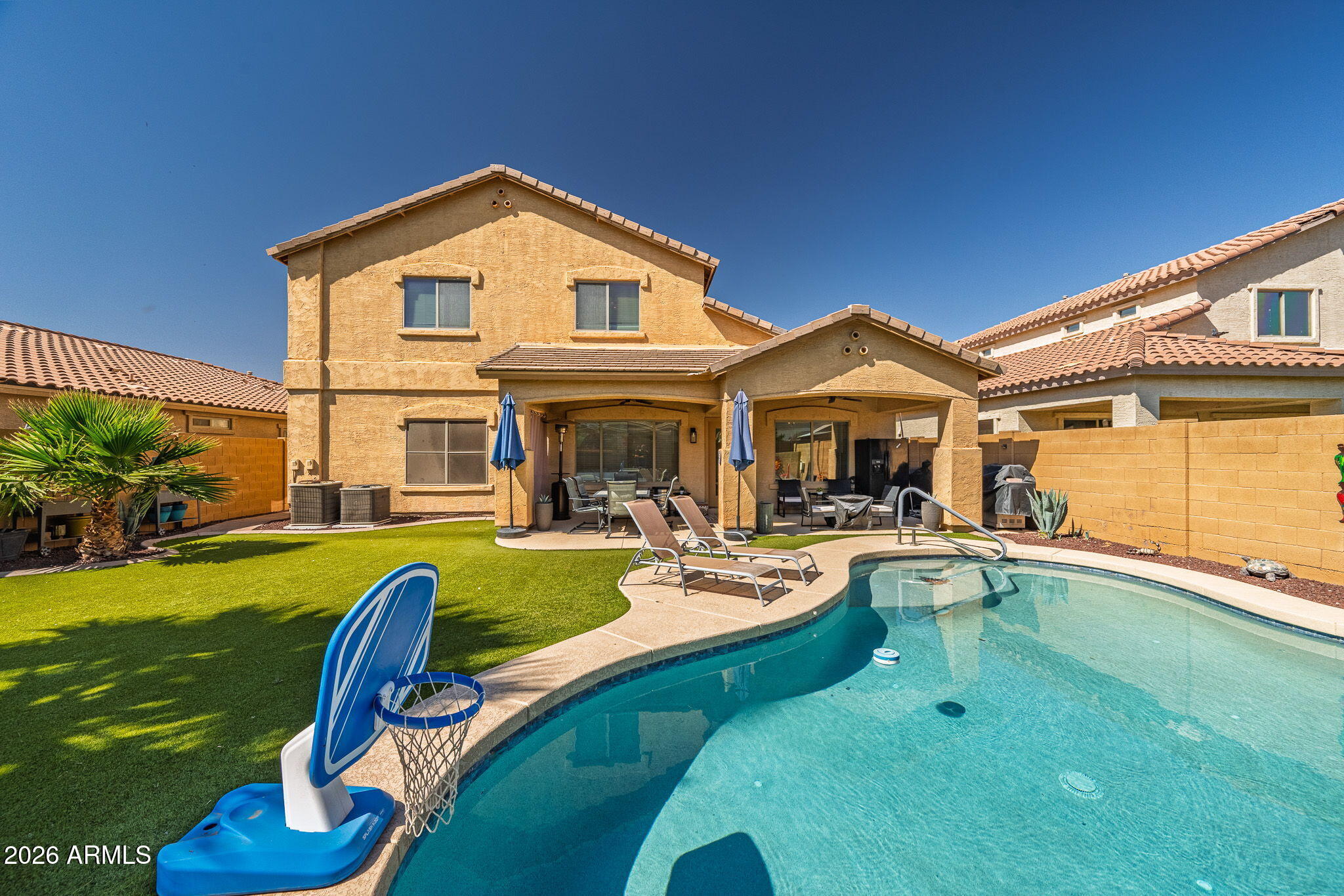Free 1 Year Home Warranty included if closed by June 30th. This home has space for everyone! With 6 bedrooms and a den with double doors this could be 7 bedrooms! The layout is anchored by two primary suites, one conveniently located on the main level and a second retreat upstairs, making it an ideal setup for multi-generational living or a grand guest room. Upon entry, you are greeted by a large formal living and dining room combo that provides a flexible area for a game room or traditional entertaining. The main family room serves as a comfortable central hub, featuring a sleek floor to ceiling tile feature wall with an integrated electric fireplace. The kitchen is equipped with two-toned cabinetry, granite countertop, stainless steel appliances and a large island with breakfast bar that overlooks the living area, all tied together with wood style flooring.  Outside, the backyard serves as a private oasis with a sparkling swimming pool. The low maintenance yard is finished with high quality artificial turf and desert landscaping, while the large covered patio provides plenty of shade for outdoor dining with a professional misting system. With a spacious two car garage and a layout that prioritizes both private retreats and open gathering spaces, this property offers a level of flexibility that is rare to find in the Maricopa market.