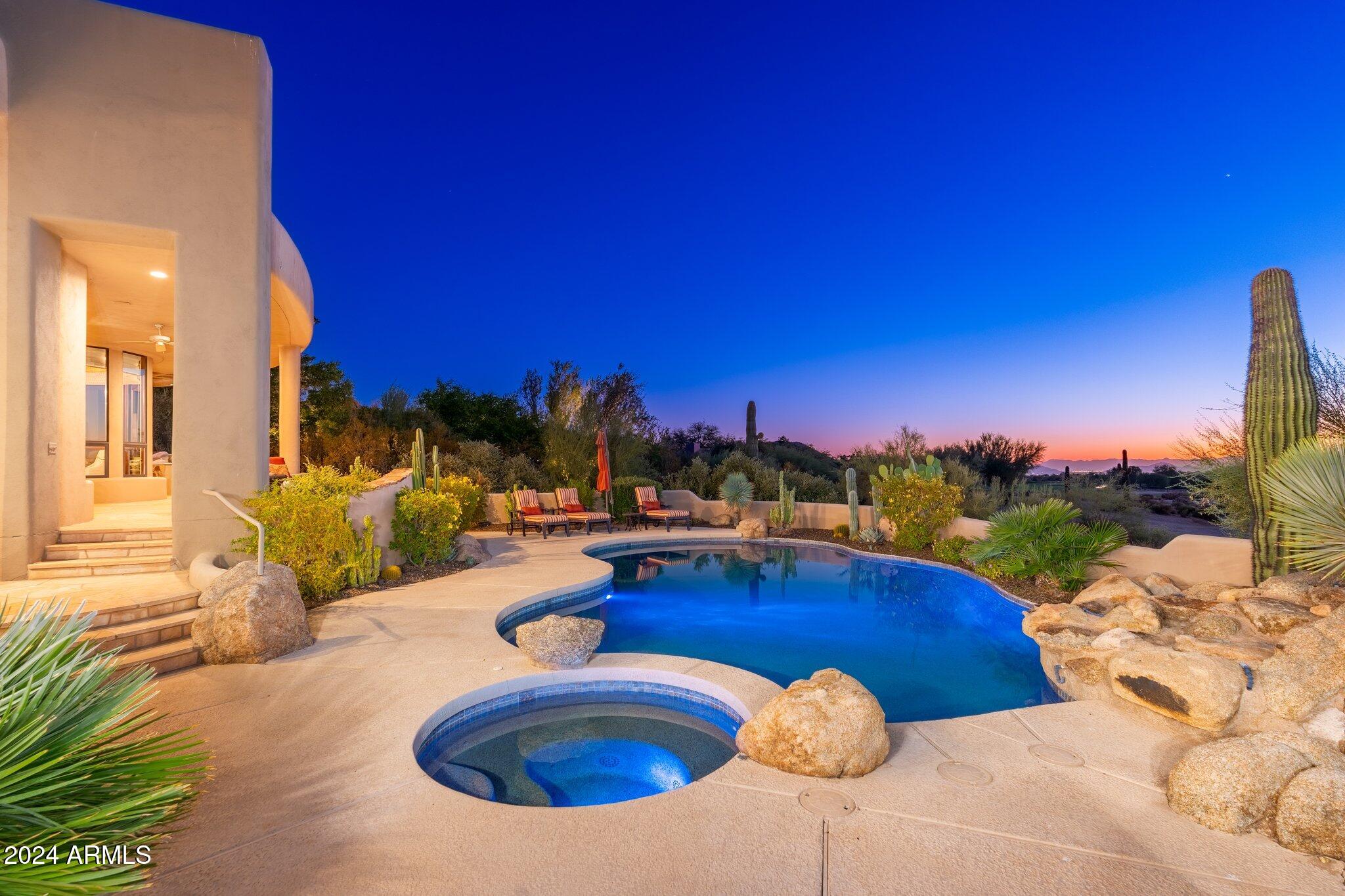 Nestled within the exclusive gated community of Windy Walk Estates at Troon Village, this exceptional home offers a rare and sought-after location custom-built by Shiloh Homes and designed by Lee Hutchinson. Situated on the 8th tee box of Troon Country Club's private course, this property boasts breathtaking city light, Pinnacle Peak, and double fairway views from the backyard, while the front showcases the majestic Troon Mountain. The positioning of the home has been thoughtfully designed to provide an idyllic setting for both relaxation and entertainment.
The outdoor oasis is a true haven, featuring an elevated covered patio with a charming fire pit, a sparkling pool adorned with a rock waterfall, a rejuvenating spa, and flagstone hardscape that adds a touch of sophistication. A Kiva fireplace and a built-in barbecue complement the outdoor space, creating an inviting atmosphere. The low-maintenance desert landscaping enhances the property's allure, ensuring a perfect blend of natural beauty and convenience.
Step inside, and you'll discover a home that has undergone a complete transformation. Meticulously remodeled to open up spaces within, the interior boasts tasteful finishes and a modern design. The custom kitchen is a chef's dream, with a large center island, designer touches, and top-of-the-line appliances, including a Subzero fridge with arched wood and iron cladding, and Wolf gas stove. The kitchen seamlessly connects to the family room, where a stone-clad fireplace becomes the centerpiece, offering valley views through dual double doors. The living room features beamed ceilings, another stone-clad fireplace, a built-in wood display unit, and even more view windows!
The well-designed floor plan encompasses four ensuite bedrooms and a private office, providing ample space. The primary suite, located on the main level, offers exterior patio access and a luxurious bath retreat with custom cabinetry, dual vanities, a large soaking tub with a picture window, a private steam shower, and an oversized walk-in closet with enough room for an exercise area. The office is adjacent to the primary bedroom and has a built-in desk and shelving. The two other ensuite bedrooms on the main level are split from the primary and office. The upper level hosts the fourth bedroom with a private balcony that captures breathtaking views.
Additional features include a formal dining room, a spacious laundry room, and a private powder room for guests. The warm contemporary Southwestern architecture, three-bay garage with attached cabinets and storage room, and impressive cacti accents complete the picture of this stunning residence, making it a truly exceptional place to call home.