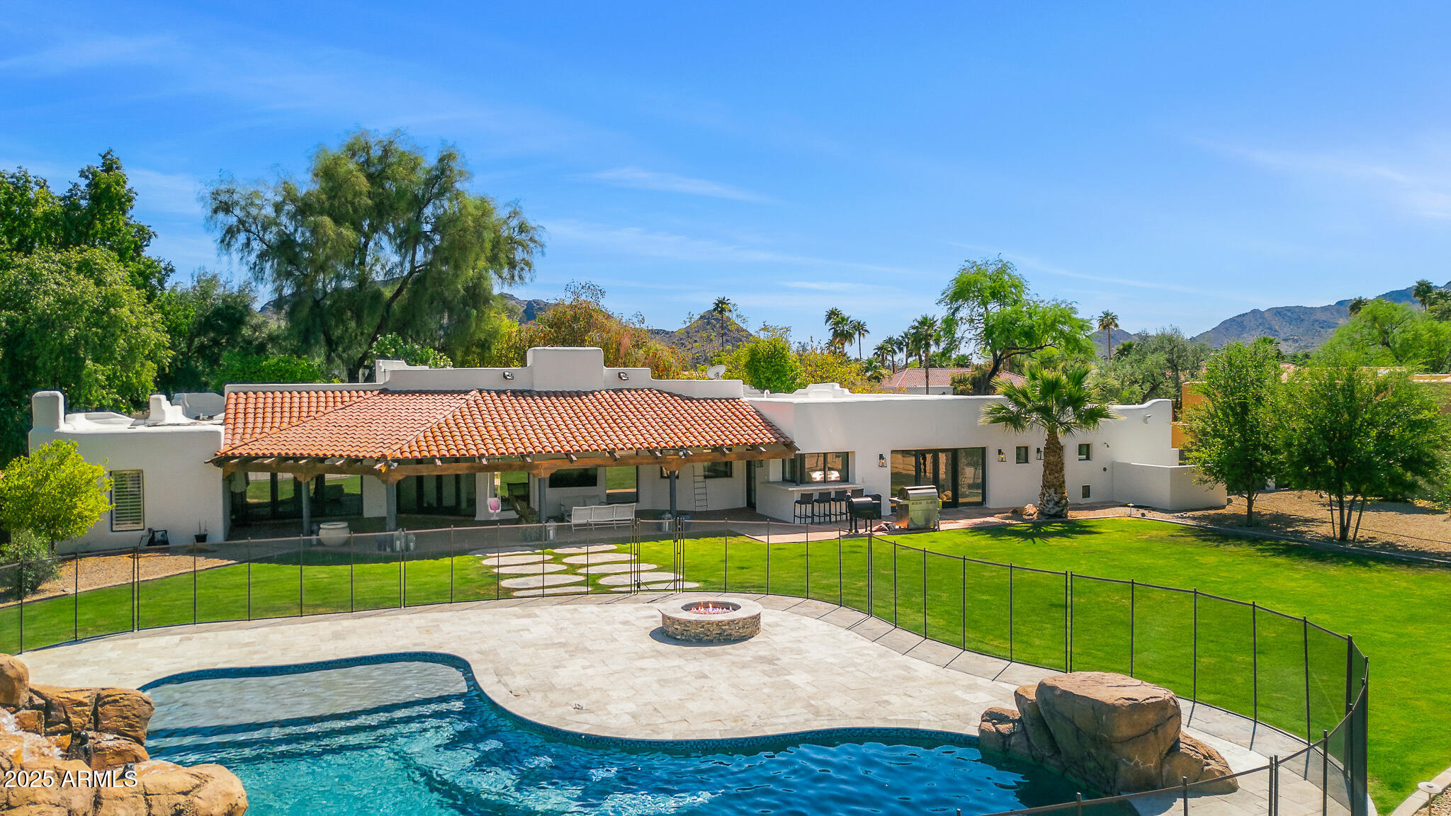 Nestled in a tranquil neighborhood of Camelback Country Estates, this stunning Santa Fe style with modern touches, combines luxury and comfort in a peaceful setting. With porcelain wooding flooring and soaring ceilings throughout, this home offers a bright and open atmosphere, enhanced by three newly remodeled bathrooms. The resort-style backyard is an entertainer's dream, featuring a spacious pool with rock features, a slide, and waterfalls, all surrounded by lush landscaping with fruit and palm trees. Expansive green grass invites play and relaxation, while the covered wood-beamed patio offers a perfect spot to unwind and enjoy the serene surroundings. The newly remodeled chef's kitchen boasts a large island and ample cabinetry, offering plenty of storage space for daily living.