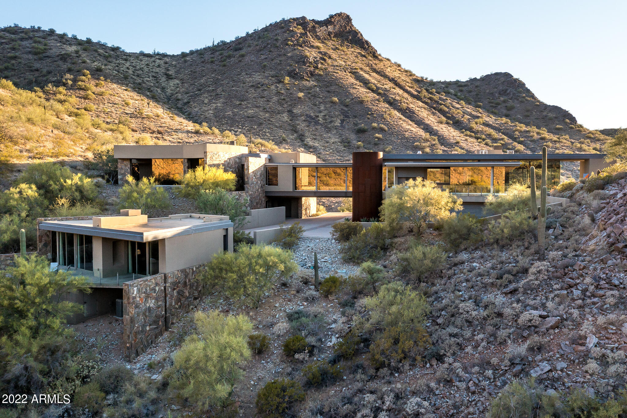The Bridge House, one of the most significant contemporary homes in Arizona, can now be yours. Located in the exclusively private guard gated community of Lost Canyon, the home sits perched on 13+ commanding hilltop acres, with 360 degree encompassing views of the surrounding McDowell Mountains. Created by the exceptional team of Allen + Philp Architects, Linthicum Custom Builders, and interior designer David Michael Miller, the home provides a natural and quiet aesthetic that beautifully fuses the surrounding Sonoran Desert with the stunning architecture. The floor-to-ceiling walls of glass, locally quarried stone walls, Bulthaup stainless steel kitchen, custom millwork, concrete flooring, cast bronze entry stairs, infinity-edge swimming pool, and endless unique details are unsurpassed.
