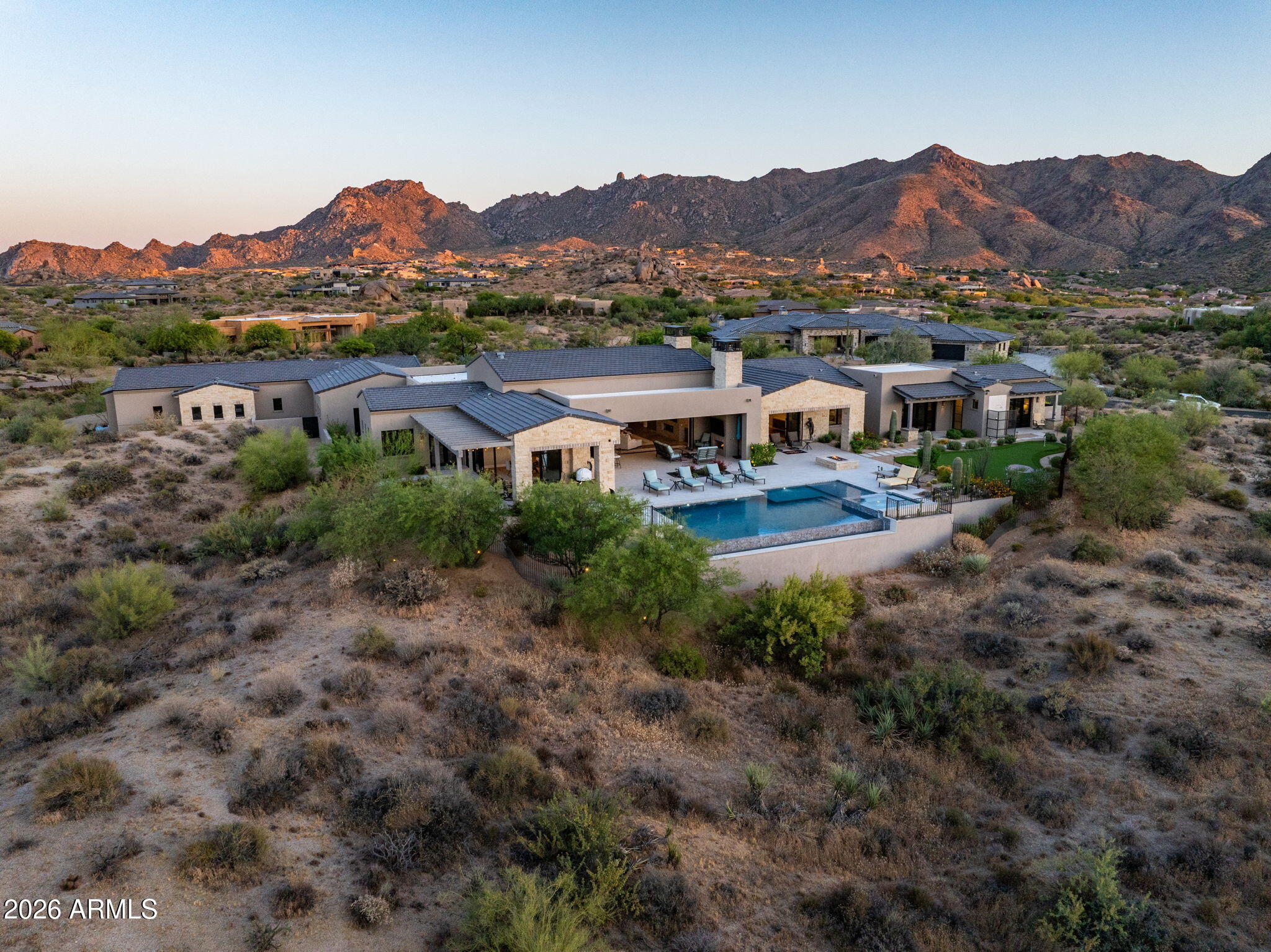 Located within the exclusive gated enclave of Sonoran Crest Estates at Rolling Hills, this newly completed Transitional Estate is perched on an elevated homesite on the east side of Troon, capturing sweeping panoramic views of the McDowell Mountains, Troon Mountain, city lights, and the Valley beyond. Built by Lineage Homes and completed in April 2024, the residence offers 10,408 square feet under roof and was thoughtfully designed for elevated entertaining and seamless indoor-outdoor living. Expansive retractable glass walls, a chef's kitchen, cantina bar, formal dining room with glass wine display, spa-inspired primary suite, oversized 5-car garages, a 136-inch Micro LED video wall, and negative-edge pool and spa all create the finest luxury living experiences Scottsdale has to offer... This property is complimented by expansive retractable walls of glass which create a true indoor/outdoor experience, connecting the great room and chef's kitchen directly to the outdoor lounge, cantina bar, pool, and entertainment areas.

The gourmet kitchen showcases an oversized island, premium stone surfaces, custom cabinetry, Wolf and Sub-Zero appliances, dual dishwashers, built-in coffee system, Kohler farmhouse and prep sinks, under-cabinet lighting, and a spacious breakfast nook. Adjacent to the kitchen, the signature cantina bar features bi-fold serving windows opening directly to the patio, complete with a beverage refrigerator and Scotsman ice maker for effortless entertaining. A temperature-controlled glass wine display, oversized walk-in pantry with custom built-ins and full-size refrigerator, and formal dining room complete the main entertaining spaces.

The luxurious primary suite offers a private retreat with fireplace, direct backyard access with Mountain Views, spa-inspired bath, oversized soaking tub, dual-head walk-in shower with rain and body sprays, designer finishes, expansive custom closet, and private laundry within the suite. Additional accommodations include three ensuite guest bedrooms and a private two-room guest casita with separate courtyard entry, kitchenette, designer bath, built-in refrigerator, and microwave.

Designed with both comfort and performance in mind, the home features high-end wood flooring, Santa Fe textured walls, solid Alder interior doors with Ashley Norton hardware, Lutron lighting controls, multi-zone Lennox HVAC systems, reverse osmosis and water softener systems, tankless hot water systems, in-ceiling fire sprinklers, and a fully integrated smart home infrastructure with multi-room audio, 7.1 surround sound, security pre-wire, surveillance pre-wire, and smart home/iPad control station control -4 integration.

One of the property's standout features is the extraordinary custom AV package, highlighted by a stunning 136-inch Micro LED display system that creates a true private cinema and sports lounge experience rarely found in residential properties at this level.

Outdoor amenities rival those of a private resort, highlighted by a superior outdoor audio system unlike anything else on the market. The resort-style backyard features a heated negative-edge pool and raised spa with Pebble Sheen finish, oversized Baja shelf, automated Pentair controls, upgraded high-performance pool systems, outdoor kitchen, fire pit, outdoor fireplace, outdoor shower, expansive travertine patios, premier landscape lighting, and a private putting green with bunker.

Car collectors and enthusiasts will appreciate the oversized insulated 5-car garage with epoxy flooring, extensive custom cabinetry, lift capability for up to 10 vehicles, 400-amp electrical service, and integrated high speed Autel Level 2 smart EV charging station.

Additional highlights include custom private gated entry, iron view fencing, premier window tint package, custom security roller shades, aluminum-clad Low-E windows, decorative paver driveways and walkways, and lush professionally designed landscaping throughout the estate grounds.

This is a rare opportunity to own a newly completed North Scottsdale luxury estate that perfectly blends elevated design, advanced technology, resort-style amenities, and premier access to Scottsdale's finest golf, dining, and lifestyle experiences.