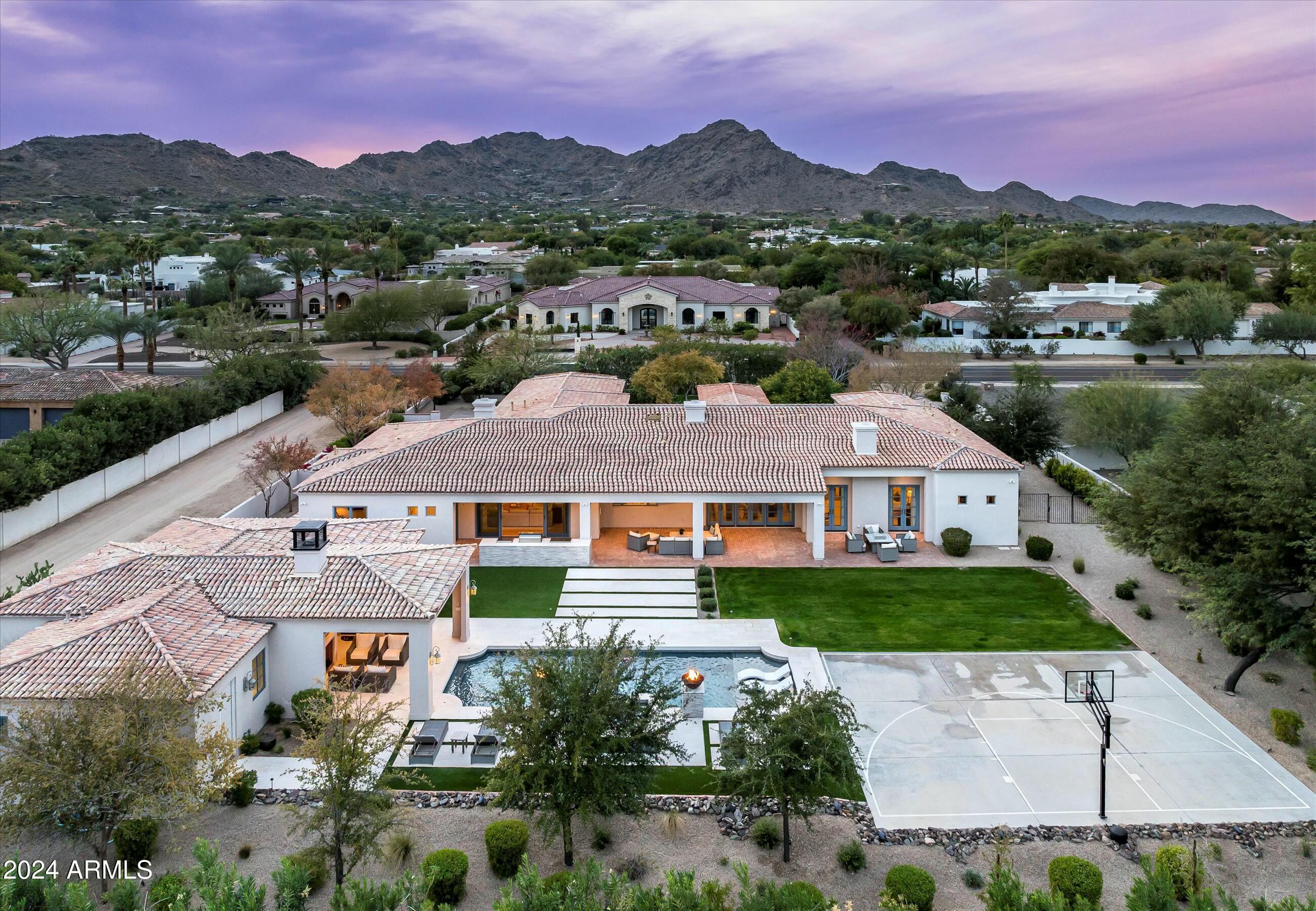 Enter into the essence of Santa Barbara, fully re-imagined with a clean and coastal feel to welcome the most savvy of buyers. An elegant entry ushers you into a spacious living room with a panoramic view of this near Paradise Valley acre & mountains beyond.  Elegant floors, coffered ceilings & a stone fireplace anchors this elegant residence.  Formal dining is enhanced by a  chilled wine cellar with a butler's pantry//bar nearby. This incredible kitchen has just been created to meet any gourmet chef's needs, complete with a massive marble island, cabinet front appliances, 2 dishwashers & automated disappearing spice racks from above. This split plan features a primary wing with an office, exercise studio (could be massive closet) while 2 additional en suite bedrooms are in the main home. A newer guest house meets multi-generational or guest needs with a complete en-suite bedroom and elegant living area adjacent to a separate game room anchored by an outdoor fireplace. Separate entrances here mean 2 different areas can be enjoyed simultaneously! This resort-style backyard is rounded out with an outdoor kitchen, sport court, sparkling pool & spa, grassy yard.  Walk to Camelback Country Club for breakfast or the prestigious forthcoming Ritz Carlton for Paradise Valley living at its very finest!  Mockingbird is among the most prestigious addresses in esteemed Paradise Valley and this enchanting residence sits right in the heart of this sought after locale. No costly HOA dues!