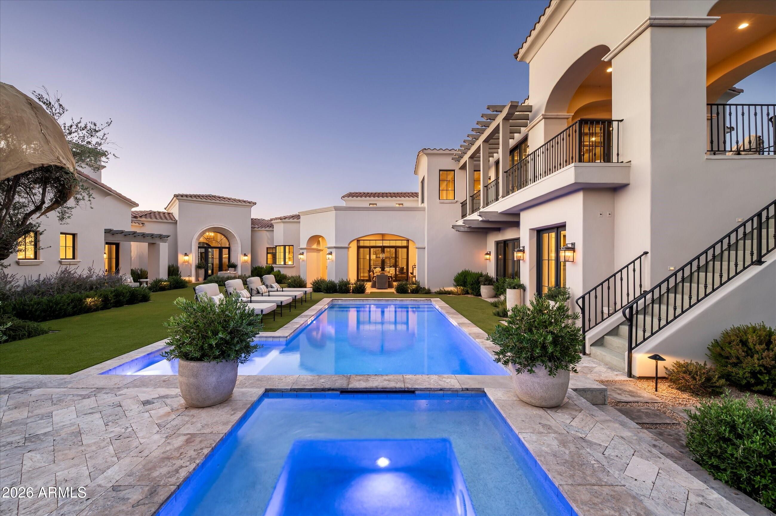 Welcome to an extraordinary corner-lot estate within the prestigious gated community of the Island at Fulton Ranch, where scale, craftsmanship, and setting converge in truly remarkable fashion. Upon arrival, lush, meticulously manicured grounds designed by award-winning landscape architect Greey Pickett create an unforgettable first impression, establishing the residence's sense of grandeur before you ever step inside. Beyond the impressive double iron front doors, a dramatic foyer immediately reveals sweeping sightlines to a tranquil fountain reclaimed from France, as well as a sparkling pool and community lake, evoking the ambiance of a private Spanish estate. Thoughtfully designed to balance elegance, privacy, and everyday livability, the expansive split floor plan offers a serene retreat within the southeast Valley's most coveted enclave.
One wing of the residence is dedicated to refined privacy and retreat, anchored by a beautiful executive office appointed with custom storage, striking windows, double glass doors, and a bespoke tri-ceiling detail. An elegant powder bath with refined finishes further enhances this thoughtfully designed wing. The primary suite is a true sanctuary, introduced by authentic wood-beamed ceilings, a stunning chandelier, a fireplace, and French doors that open to a private pergola-covered patio. Equally impressive, the palatial primary ensuite is appointed with dual vanities, a freestanding soaking tub overlooking serene outdoor views, an oversized walk-in shower with dual and rain shower heads, and two custom walk-in closets, creating an atmosphere of exceptional comfort and sophistication.
The opposite wing of the residence is designed for both impressive entertaining and elevated everyday living, anchored by a magnificent great room with soaring ceiling heights, beautiful, authentic wood beams, a grand chandelier, and a dramatic fireplace. Double sliding French doors open directly to the backyard, creating a seamless connection between the interior living spaces and the resort-style outdoor setting. The great room flows effortlessly into the gourmet kitchen, where a massive center island serves as the centerpiece, complemented by a Wolf 6-burner cooktop, Wolf professional-grade vent hood, built-in wall ovens, a double Sub-Zero refrigerator, custom cabinetry, and elegant Carrera marble. Just beyond, the butler's pantry offers abundant storage and a convenient beverage station, enhancing the home's entertaining capabilities. 
This wing also includes two beautifully appointed guest suites, each with its own ensuite bath, positioned around a flexible living space for added versatility. Down the hall, an additional guest room, currently used as a home gym, is complemented by a full bathroom. Equally thoughtful in design, the spacious laundry room is appointed with dual washers and dryers, a utility sink, abundant custom cabinetry, and elegant Carrera marble countertops with tile finishes. Upstairs, a spacious lounge with built-in storage and a beverage refrigerator provides an inviting gathering space, while the dedicated home theater with built-in surround sound and a movie projector creates an exceptional cinematic experience. An additional guest suite with a private ensuite bath enhances the flexibility of this level, which opens to a covered wraparound balcony showcasing incredible views.
The spectacular backyard evokes the ambiance of a private Mediterranean villa, framed by an imported heritage olive tree, unobstructed lake views, and the rare privacy of having no rear neighbors. Designed for resort-style living, the outdoor retreat features a sparkling pool and spa, a fully equipped gazebo with built-in BBQ and sink, and multiple covered and open-air spaces for lounging and entertaining. Accessible from several sets of beautiful sliding French doors throughout the home, the backyard creates a seamless indoor-outdoor experience, while a professional-grade misting system provides year-round comfort.
Experience the pinnacle of luxury waterfront living in Fulton Ranch, where timeless architecture, exceptional amenities, and breathtaking views come together to create a truly remarkable place to call home.