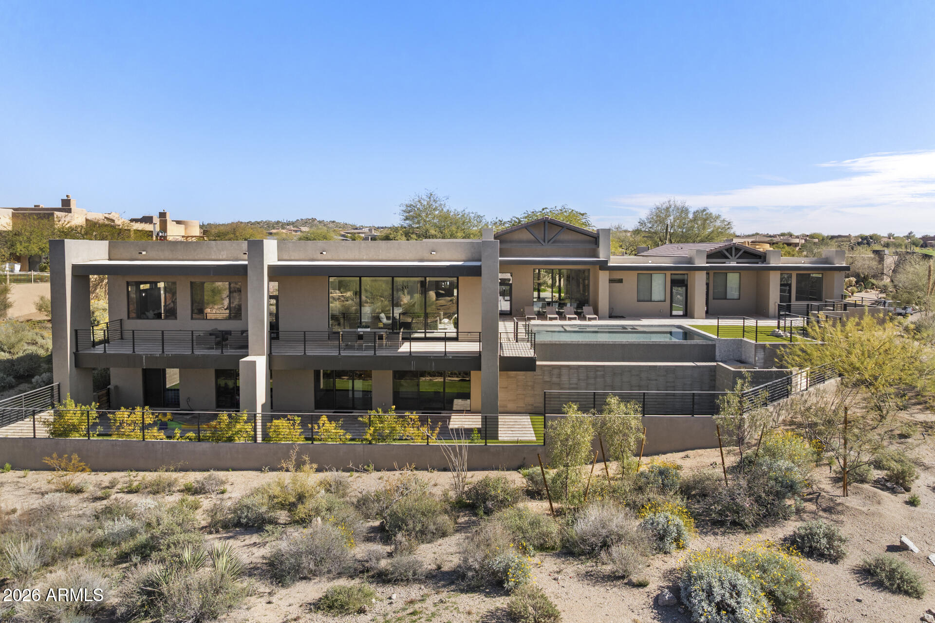 Located within the gated Talus community at Troon North, 29599 N 106th Place is a modern desert estate that strikes a rare balance between scale, design, and livability. Built in 2022 and perfectly tucked into an acre lot, the home lives primarily on a single level, with what feels like an entirely separate residence downstairs, ideal for entertaining, kids' play areas, or hosting extended guests. At nearly 9,700 square feet, this home truly checks almost every box, offering exceptional size, setting, and one of a kind thoughfullness behind the layout and functionality. A 12-foot glass pivot entry sets the tone, opening to interiors with dramatic 16-foot ceilings and expansive walls of glass. Dual 20-foot sliding doors connect the main living spaces to the outdoors, filling the home with natural light and framing desert and mountain views. The architecture is clean and contemporary, with a palette that can be easily customized to feel like home for any buyer.

The kitchen sits at the center of the home and is built for gathering, featuring dual oversized quartzite islands, Thermador/Wolf appliances, two dishwashers, and a full butler's pantry. The connectivity and flow from indoors to out define Arizona living at its best.

The owner's suite is a private retreat with a fireplace, spa-style bath with soaking tub and walk-in shower, and a custom dressing room. Four additional en-suite guest rooms, along with an attached casita, provide unmatched flexibility for family and guests alike.

A dedicated office, media room, gym and expansive downstairs living area add versatility for work, recreation, or entertaining on a larger scale.

Outside, the backyard is designed as a true retreat with a heated negative-edge pool and spa, travertine pavers, turf, and multiple covered patios. A nearly 800-square-foot view deck captures elevated desert and mountain vistas, essential to the Troon North lifestyle.

This home is a standout example of luxury modern desert living. The value offered through the sheer size, layout, and lot makes this a must-see opportunity.