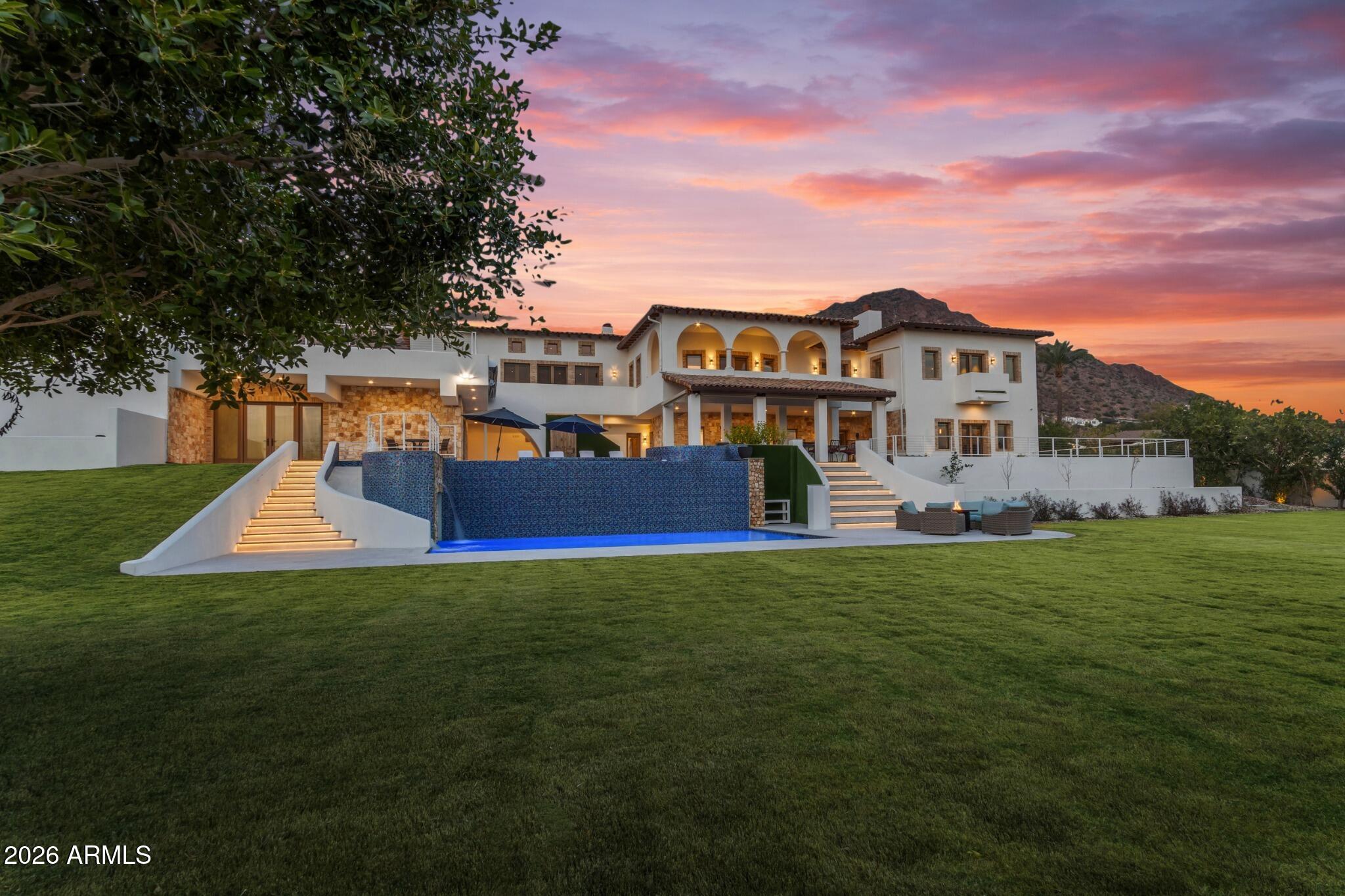 Privately gated on over 1.09 acres in prestigious Arcadia Proper -one of Phoenix's most sought after neighborhoods. The Rockridge Estate captures panoramic views of the city skyline and Camelback Mountain as its backdrop. A grand porte-cochère arrival leads to soaring, architecturally rich interiors, where a dramatic 15' wall of glass frames the view. The resort-style backyard is anchored by a two-level infinity-edge pool with a 10' water wall, grotto, and water slide. Spanning over 13,000 sqft, the estate offers 7 bedrooms, including two primary suites, 9 bathrooms, 5 fireplaces, an elevator, and expansive living spaces designed for elevated living and entertaining. The chef's kitchen serves as the heart of the home, appointed with Wolf and Sub-Zero appliances , dual cooking surfaces, and a curved run of custom cabinetry and quartzite countertops beneath a wall of windows. An expansive multi-level island, farmhouse sinks, and walk-in pantry are complemented by a secondary pantry, laundry, mudroom features, and dedicated dog spa.
The upper level, accessed from the beautiful wrought-iron railed grand staircase, or private elevator, offers a loft overlooking the main living areas and a north-facing veranda capturing Camelback views. A game room with wet bar, fireplace, en-suite bedrooms, and optional private access creates a flexible secondary living environment.
The upper-level primary suite spans approximately 2,000 sqft with fireplace, terrace, and sweeping views, complemented by a spa-inspired bath, boutique-style closet with laundry, and adjoining flex space. A rotunda office or studio and lower-level vault with wine cellar or simulator potential add further versatility.
Lush, park-like grounds unfold across multiple levels with illuminated staircases and expansive terraces. A striking two-level infinity-edge pool cascades over a 10-foot water wall, with a lower-level grotto, water slide, and lounge areas, and an upper level featuring an infinity-edge spa spilling into both tiers, in-water seating, and sun shelf. A covered patio with BBQ and bar seating for 12, motorized shades, and custom awning supports year-round enjoyment. An elevated deck and rooftop lounge capture panoramic city, mountain, and 360-degree views -creating a seamless indoor-outdoor experience at every level.
An attached two-car garage is complimented by a detached RV garage with additional bays, accommodating 10+ vehicles, recreational storage, or car collections. A dedicated RV gate and expanded parking areas maintain the integrity and flow of the grand circular drive.
Set at the base of Camelback Mountain in Arcadia Proper, with close proximity to premier dining, shopping, and lifestyle amenities.