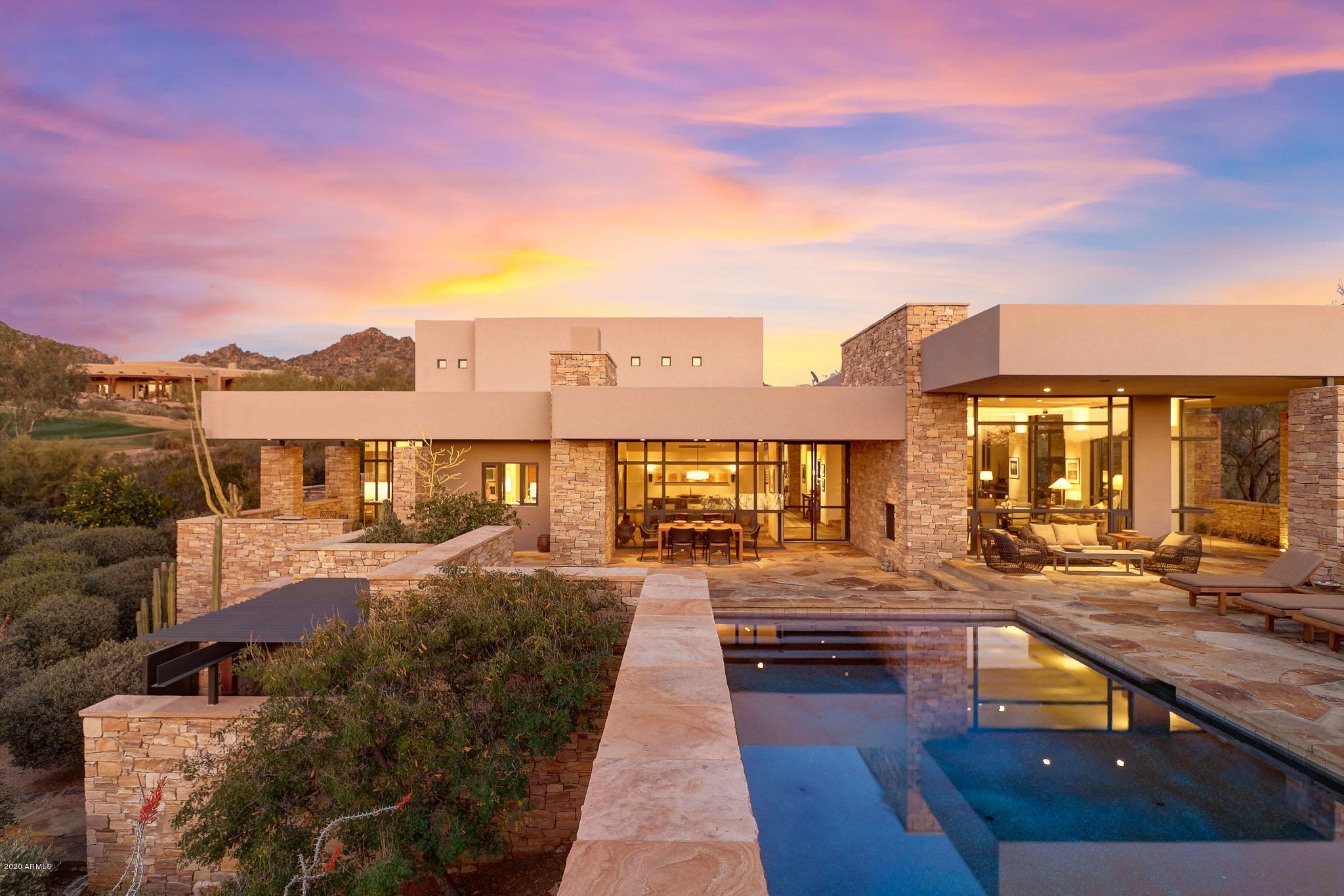 Timeless architecture and design grace this contemporary styled home with beautiful organic elements throughout. This masterpiece is located in the prestigious guard-gated community of Glenn Moor at Troon Village, home to the back nine of Troon Country Club's private course. Featured in Phoenix Home and Garden Masters of the Southwest issue, the home was designed by renowned architect Hugh Knoell (Knoell Quidort Architects) and offers design elements that embrace the desert setting allowing for seamless living inside and out including steel and glass doors, flagstone flooring throughout, high ceilings, locally sourced stacked stone walls and clean lines. The home features a main level master with a spa-like bath including a private vanity area, large soaking tub and a dual entry shower. Upstairs finds two additional guest bedrooms with shared bath featuring basket weave tile accents, dual sinks and a separate shower/toilet room opening to the loft with built-in entertainment center. Two more ensuite guest rooms can be found in the detached guest house with a private laundry and views overlooking the surrounding McDowell Mountain range, Pinnacle Peak and Troon Mountain, golf course, and pool offering a resort style experience for visiting guests. The lush, superbly designed landscaping continues the organic desert feel with numerous species of succulents, cacti, trees and boulders surrounding the decomposed granite driveway. The impressive entryway showcases a full length 40-foot long water feature and a direct view of the entry with a suspended staircase and a perfect neutral palette. The backyard embraces the private setting with a negative edge pool and spa reflecting the famous Arizona sunsets and local foliage for a truly one-of-a-kind experience. Flanked by two additional side patios, the outdoors is a perfect setting for entertaining guests with al-fresco dinners and lounging in the splendid weather all while admiring the distant city light views. Back inside the home, the kitchen is a chef's delight with a Subzero refrigerator and freezer, Thermador wall oven and microwave, Viking gas stove with hood vent, and Miele coffee maker all in stainless steel. The matte finish countertops and tile backsplash bring a delicacy to the custom Hawaiian Koa wood cabinetry extended to the built-in desk at the intimate breakfast area with a wall of windows. Large gathering spaces including a dual setting great room with recessed beam ceilings, built in bookcases, floor to ceiling windows and cozy fireplace adjacent to the dining room overlooking the wall fireplace in the backyard. This home is on the market for the very first time and provides a once-in-a-lifetime opportunity to own a true piece of art that embraces luxury living with a hard to find intimate home feel at this level of design.