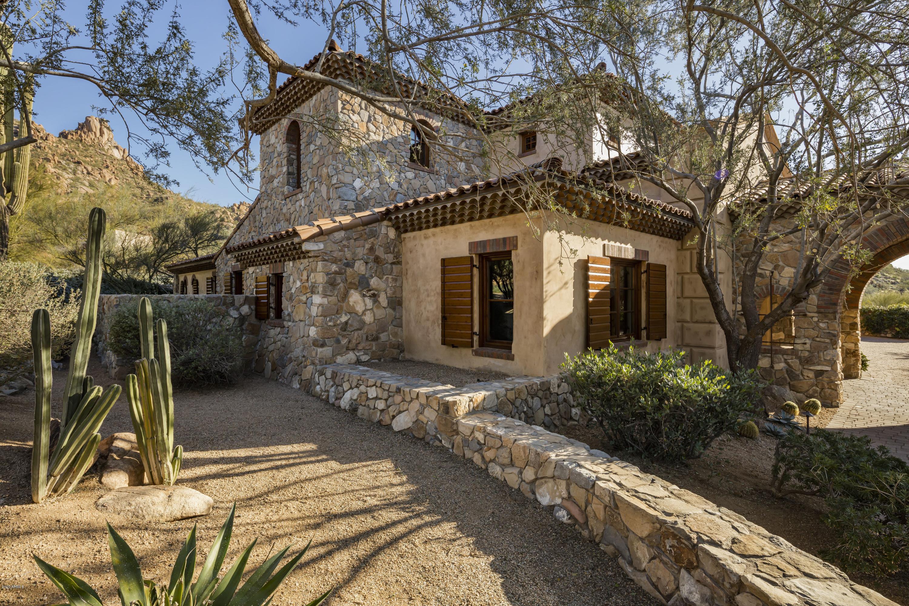 Timeless, Old World-style on a golf course lot with Pinnacle Peak and sunset views in Estancia * The architectural details blend stacked field stone, brick, wood and plastered exterior walls to create an elegant desert estate * The floor plan includes a master suite with exercise room on the main level with an additional guest suite and office/media room in the house and a detached guest house * Interior details include stone and wood plank flooring, Cantera fireplace surrounds and ceiling details that are trimmed with wood beams and paneled wood ceiling details * The living areas include an open kitchen to family room concept and a massive, separate dining and living room with soaring ceilings and multiple accordion-style doors that flow to the outdoor living space * Upstairs is an additional master suite with office and view deck * The outdoor space is highlighted by linear covered patios adjacent to the indoor living spaces, a fireplace and an open sundeck by the oversized heated pool with spa * A 3-car garage and a large, temperature controlled wine room completes the residence *