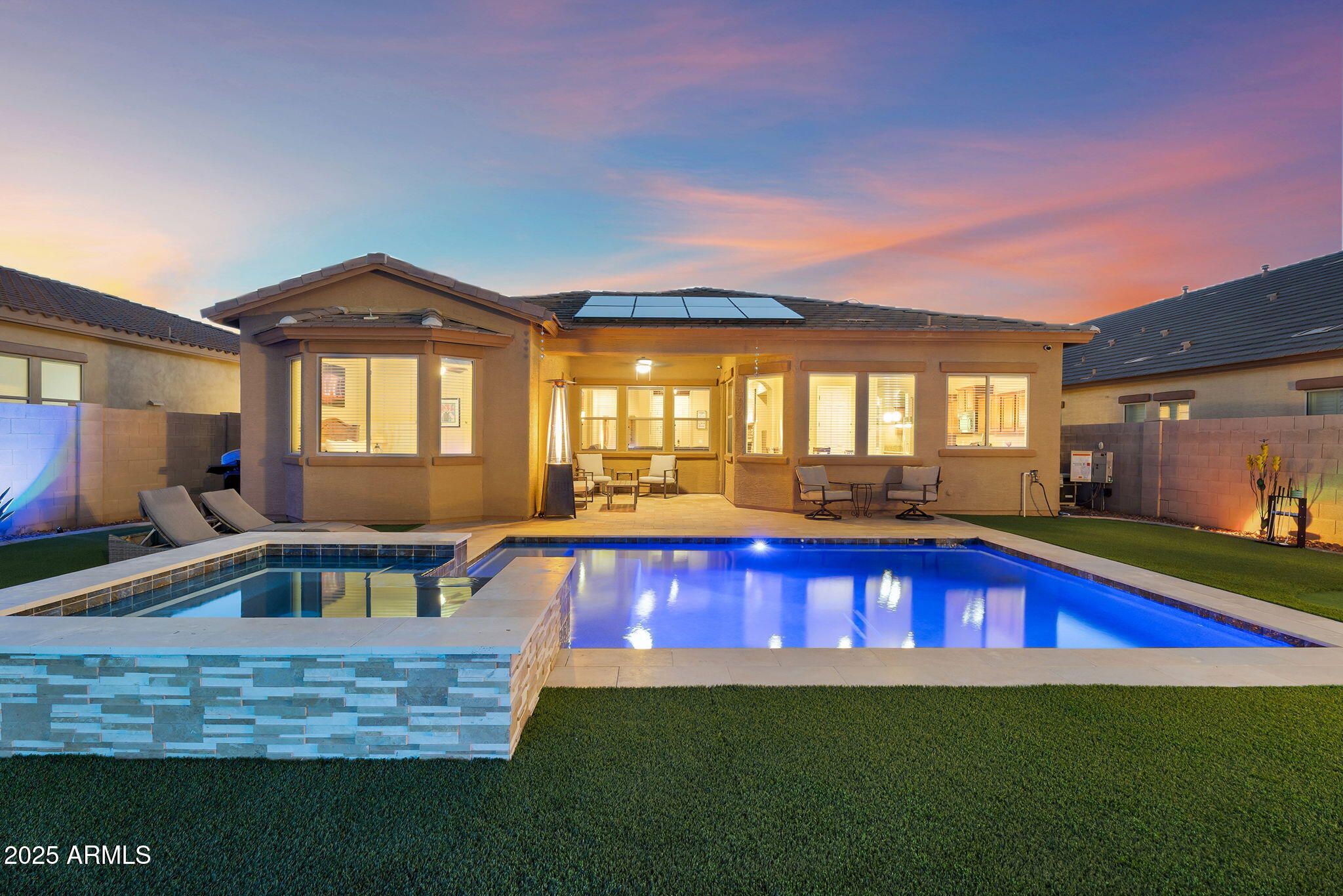 Welcome to this stunning single-story, 3-bedroom, 2-bath home located in the highly desirable Estrella Mountain Ranch community. From the moment you arrive, you'll notice the inviting stone-accented façade, beautiful desert landscaping, and rare 3-car split garage. Inside, the home is finished like a model, with formal living and dining spaces, a two-way fireplace, beamed hallway ceilings, crown molding, and abundant natural light throughout. The kitchen is both stylish and functional, featuring stainless steel appliances, granite countertops, ample cabinetry, a butlers pantry, and an island with a breakfast bar--perfect for everyday living and entertaining. The spacious primary suite offers a charming bay window and a luxurious ensuite complete with dual sinks, a separate... soaking tub and shower, and 2 walk-in closets. Step outside to a backyard designed for year-round enjoyment in the Arizona sun. The newly (2024) updated outdoor space features a heated sparkling pool and spa, a chipping and putting green, elegant travertine tile, new turf, and a covered patio ideal for entertaining, relaxing, and taking in breathtaking mountain views and unforgettable desert sunsets. Owned solar adds energy efficiency and long-term savings, making this home as practical as it is beautiful. Located within the highly sought-after Estrella Mountain Ranch, residents enjoy access to an incredible array of resort-style amenities. The community features multiple resident centers with fitness facilities, heated pools, splash pads, water slides, lounges, and on-site dining, along with lakes for kayaking and paddle boating, an award-winning championship golf course, and miles of scenic hiking, biking, and walking trails. With more than 50 neighborhood parks, community events, and stunning mountain and desert surroundings, Estrella offers an unmatched lifestyle where recreation, relaxation, and natural beauty come together. Partial Roof  Replacement (2022) & a Newer Soft Water System in 2024.