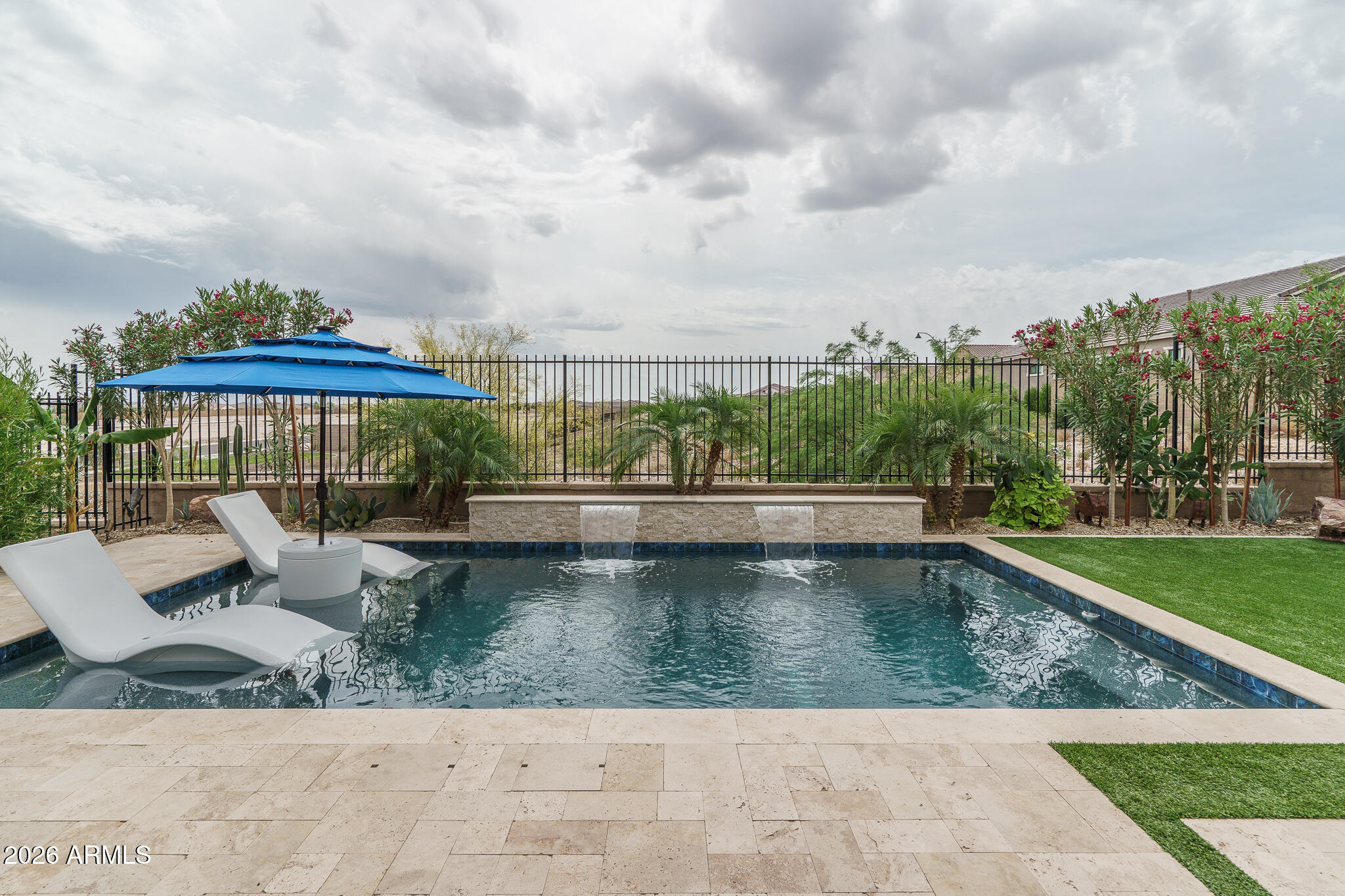 Live the active adult lifestyle of your dreams from this immaculate, highly upgraded home that sits on a premium wash-bordering lot and has mountain views from the front & backyards. The backyard features a stunning, heated salt water pool with water features and baja step, easy-care artificial turf, and a covered patio with travertine pavers. Floor plan includes 2 bedrooms, each with en-suite baths, plus a versatile den/office. The kitchen has white cabinets with crown molding, quartz counters, stainless appliances, a butler's pantry, a walk-in pantry, custom dry bar cabinets & beverage cooler, and large island with breakfast bar. The primary suite has a deluxe bath with dual sink vanity, oversized tiled shower, and walk-in closet. Guest suite also has a walk-in closet & full bath. Other features: spacious laundry room with cabinets and sink, designer light fixtures, custom slat feature wall in the dining area, a front security door, and a 2-car garage. Resort-style amenities for this 55+ community include multiple pools and spas, pickleball, tennis, a workout facility, on-site restaurant and spa (all ages welcome), two golf courses, and miles of hiking trails.  Convenient access to dining and retail shops, and easy access to Loop 303 and I-10.