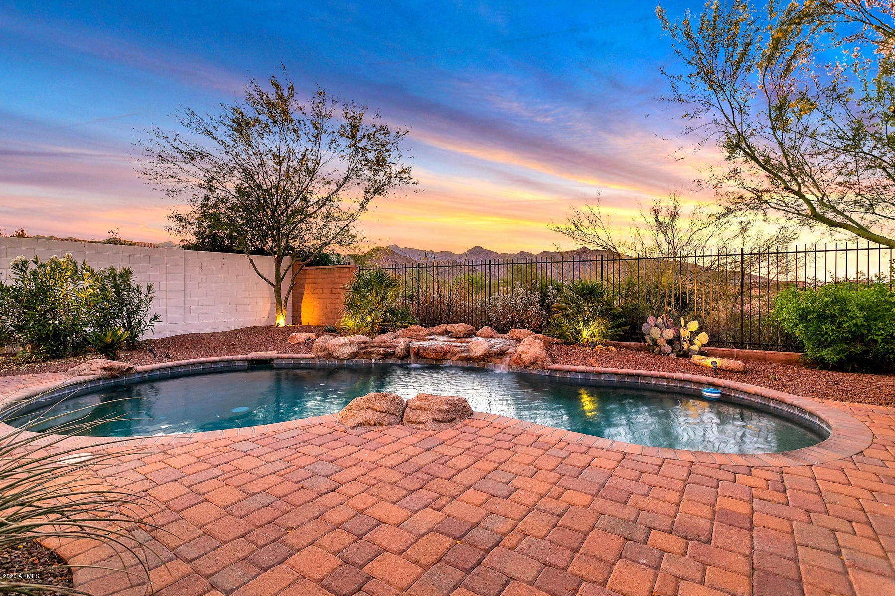 MOUNTAIN VIEWS (view fencing) from PebbleTec POOL (w/ HEATER & rock waterfall feature). Private backyard facing a WASH with an extended paver patio. Plantation SHUTTERS on all windows (except for windows with custom draperies), ''HARDWOOD'' floor tile, beautiful FIREPLACE, stainless steel appliances, SNAIL SHOWER in Primary Bath. Located across the street from Verrado elementary & middle SCHOOL, 2 blocks to SUNRISE MARKET (Haymaker, West Rose Winebar, DeGino Coffee, Bosa Donuts), and only 4 blocks to Verrado's quaint DOWNTOWN: Gratzie Pizzeria, Tempo Urban Bistro, Bashas, Orange Leaf Yogurt, Anthem Coffee, and The Center on Main (GYM and pools). 6 blocks to the Verrado GOLF COURSE (and Victory GC).