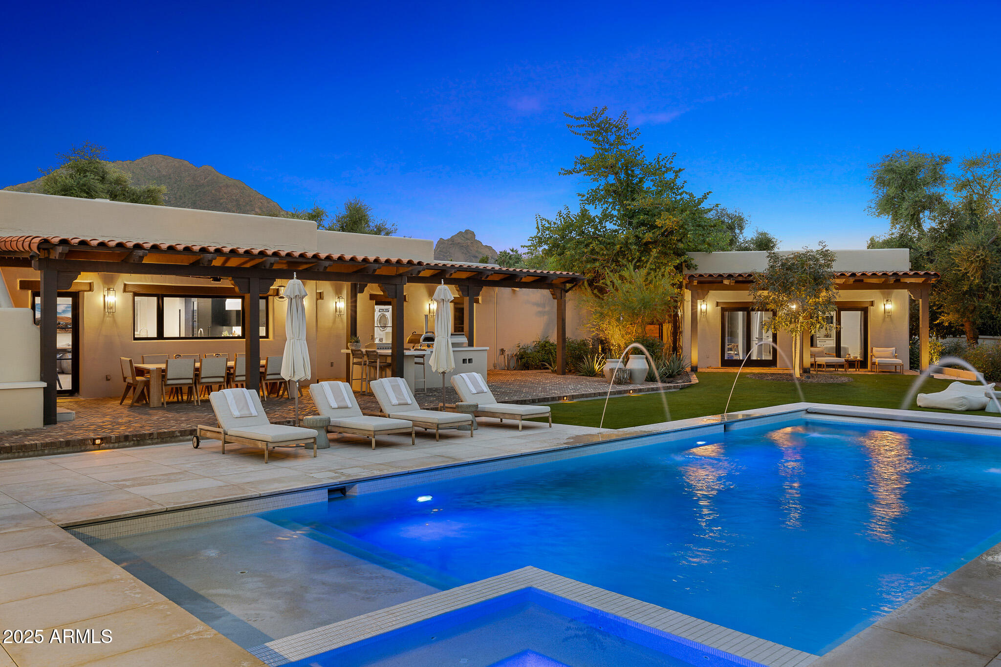 Located in the Paradise Valley's  highly coveted guard-gated community of Finisterre, this exquisite residence blends Territorial-inspired architecture with modern sophistication. Recently remodeled by Vallone Design, the home radiates timeless elegance, layered textures, and refined desert luxury.  The main house welcomes you with a spacious living room anchored by a statement fireplace and wet bar, ideal for both entertaining and quiet evenings at home. The designer kitchen is a true showpiece—featuring marble countertops, a waterfall island, top-of-the-line appliances, a charming breakfast nook, and an expansive butler's pantry that flows seamlessly into a wine room.  The oversized primary suite is a retreat of its own, complete with a cozy sitting area beside a gas fireplace, a private home office, and a spa-like bathroom with a steam shower, soaking tub, private water closet, and a generously shared closet. Two additional guest bedrooms, both ensuite, offer style and comfort for family and visitors alike.  Across the property, a detached guest house provides a private sanctuary with its own kitchenette, living space, bedroom suite, and a dedicated wellness studio featuring an infrared sauna and outdoor cold plunge.  The resort-style backyard completes this remarkable estate with a sparkling pool and jacuzzi, ramada, outdoor kitchen, and generous sport and bocce ball courtsall surrounded by lush landscaping and mountain vistas.  This is Paradise Valley living at its most refinedarchitectural integrity, modern comfort, breathtaking Camelback Mountain views and enduring elegance in one of Arizona's most exclusive communities.