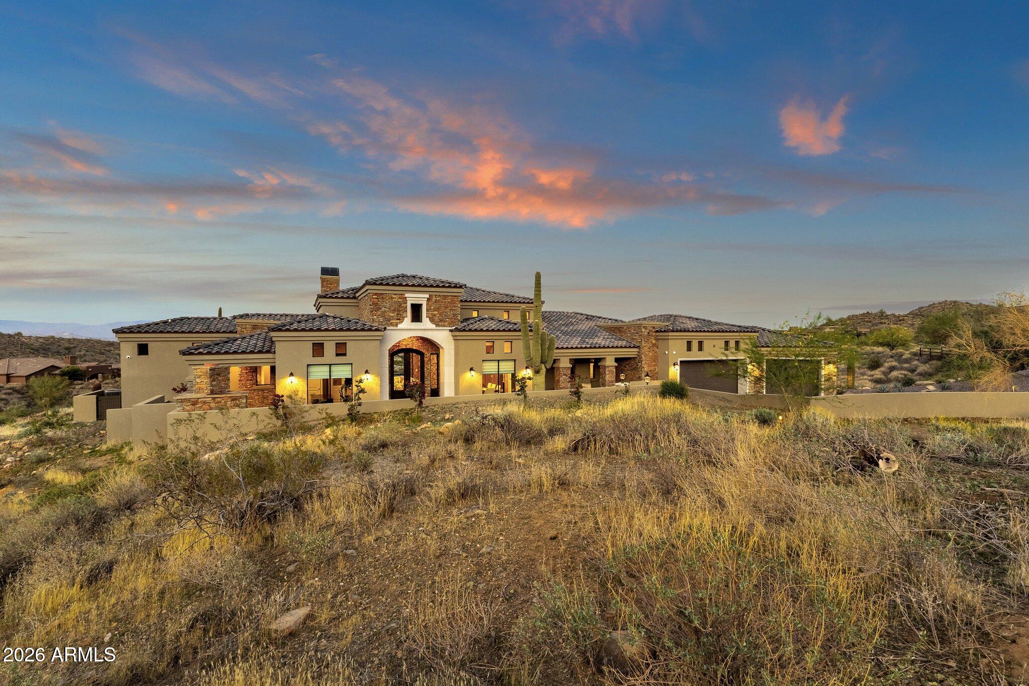 This custom residence offers exceptional privacy, desert views, and refined indoor-outdoor living in a sought-after setting. The open great room features soaring ceilings, stone accents, and expansive glass doors creating a seamless connection to outdoor living spaces. The chef's kitchen includes a large island, custom cabinetry, premium appliances, and a hidden walk-in pantry, ideal for entertaining and everyday living. Bedrooms are large and spacious, offering comfort and flexibility. The home is equipped with electric blinds, built-in WiFi, and integrated audio throughout. Outdoor living includes expansive travertine patios, covered seating areas, a built-in outdoor kitchen, fire features, and a negative-edge pool with raised spa. Enjoy sunrise views from the backyard and sunsets from the gated front courtyard with fireplace. Custom craftsmanship and thoughtful design are evident throughout.