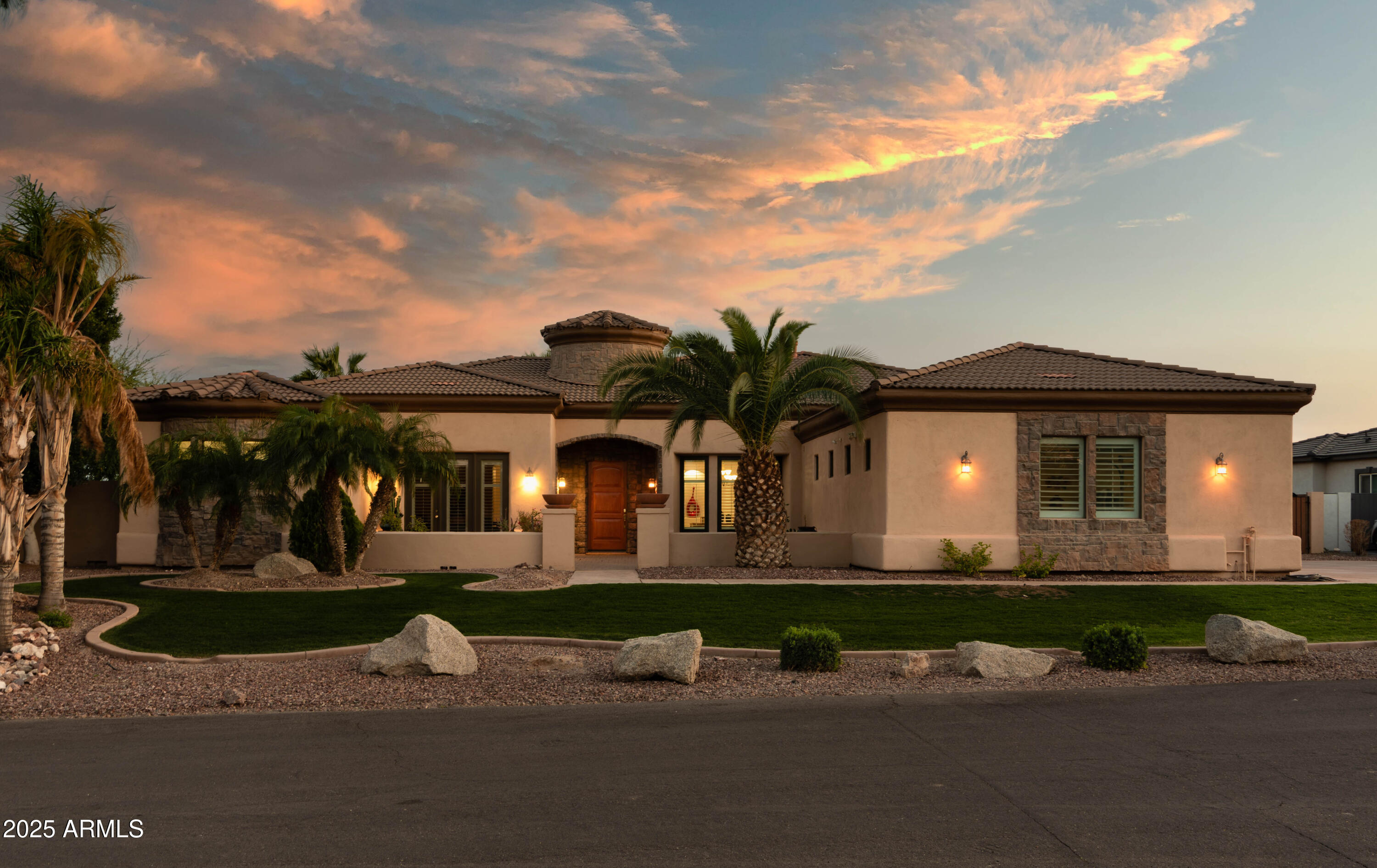 Nestled at the base of the stunning White Tank Mountains in the exclusive gated community of Russell Ranch, this elegant Tuscan-inspired custom estate sits on an oversized corner lot engineered for the modern adventurer. Designed with custom luxury & recreational freedom in mind, this rare property features a double RV gate with ample parking for your motorhome, boat, or weekend toys, plus HOA covenants provide the opportunity to build a custom detached RV garage. Step through the grand courtyard entry into over 4,000 square feet of masterfully crafted living space featuring 4 spacious bedrooms, 4.5 baths, private executive office with direct courtyard access & dual stone-clad gas fireplaces. Enjoy the spacious feeling of 12 foot ceilings throughout the interior of the home. The heart of the home is a gourmet chef's kitchen appointed with rich custom cabinetry, granite tile countertops, dual wall ovens, gas cooktop, center island with prep sink, dedicated bar with buffet area & an enclosed butler's pantry. The owner's retreat serves as a true sanctuary, boasting its own stone fireplace, French doors to the back patio, and a spa-quality ensuite with jetted tub, travertine walk-in shower & generous walk-in closet. Outside, the expansive curved covered patio overlooks a lush green lawn framed by mature palm trees, offering the perfect canvas & abundance of space to add a resort-style custom pool while still preserving your premium vehicle storage. Complete with a 3-car garage, newer interior & exterior paint & two new 5-ton, 14 SEER Goodman HVAC systems for energy-efficient comfort, this one-of-a-kind home offers an unparalleled lifestyle with easy access to scenic hiking trails, golf courses, premier dining & top-rated schools.