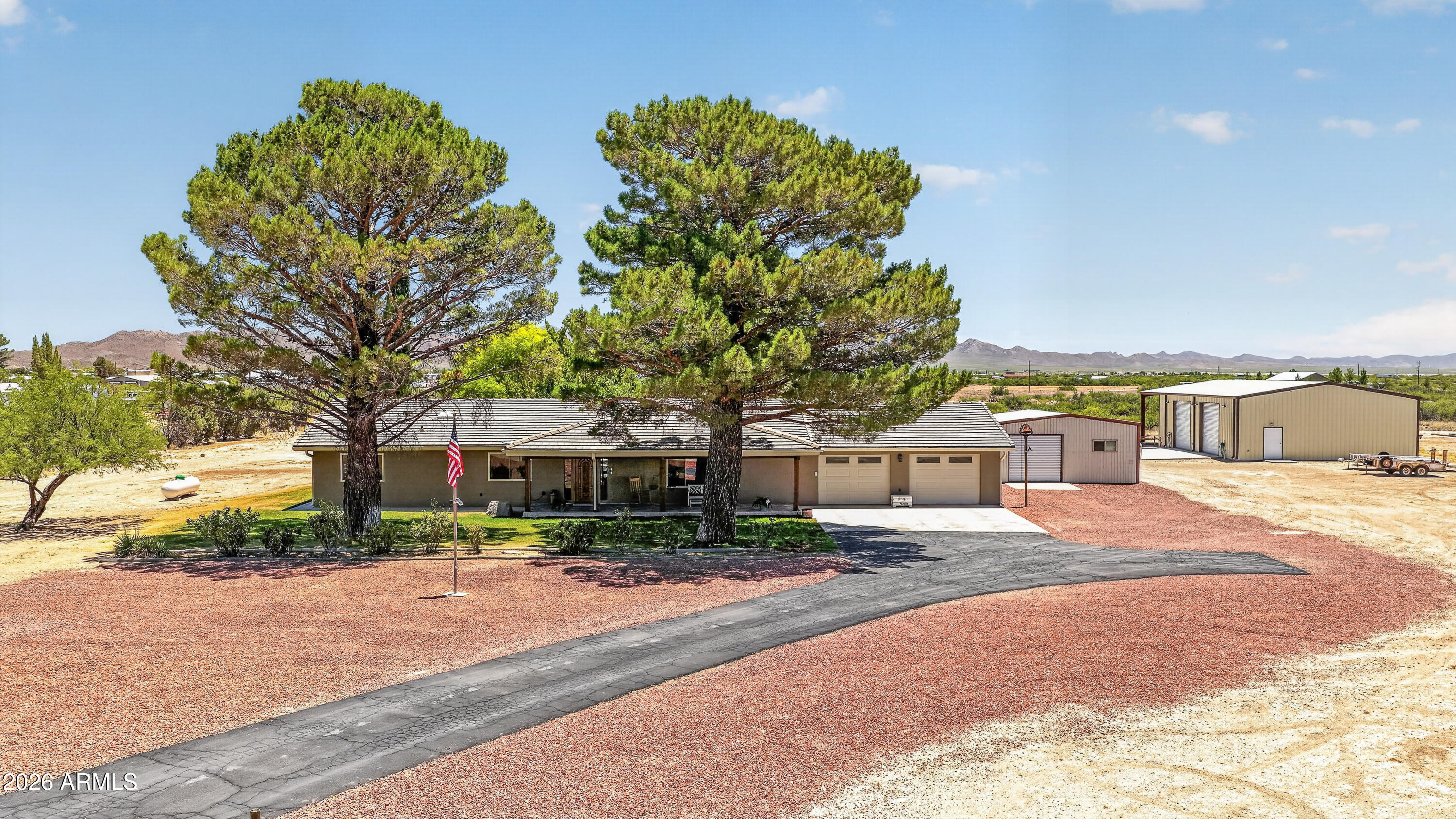 SPECTACULAR 17-ACRE WILLCOX RETREAT! Custom home w/mountain views, 50x40 insulated shop w/10,000-lb Challenger 2 post vehicle lift, RV parking w/hookups. Recently updated: NEW 2023 Tile Roof and Seamless gutters. French door fridge, Cambria quartz counters, solid wood cabinets, 6-burner propane cooktop, 2026 new carpet in Primary and Livingroom, custom shutters. Master suite w/European walk-in shower. Two covered porches. Outdoor paradise: covered patio w/fans/TV, automatic sprinklers, fruit trees, lighted batting cage. 25x25 workout facility, insulated office. 13 total parking spaces! Move-in ready! Owner/Agent - Seller is Licensed Real Estate Agent in Arizona. 1 year Home Warranty offered. Propane tank is rented from Cochise Farmers Association. Use Perla Martinez at Pioneer Title KITCHEN & LIVING SPACES
The heart of the home features a large island with electrical outlets, pendant lighting, Kenmore Elite 6-burner propane cooktop with stainless steel hood, and Kohler 60/40 deep pot sink. Built-in bookshelves and 9-foot ceilings throughout create an open, welcoming atmosphere.

BATHROOMS
Primary bathroom showcases European-style doorless shower with tile surround, built-in niches, rain showerhead, and handheld sprayer. Hall bathroom includes dual sinks and professionally refinished tub/shower with durable resin coating.

OUTDOOR FEATURES
West-facing orientation provides shaded back patio during evening hours. Mature cypress and fruit trees complement the manicured grass areas with in-ground automatic sprinkler system. Raised garden beds and block fencing with steel gates ensure privacy and functionality.

SHOP COMPLEX
The 50x40 metal shop includes 6-inch concrete slab, spray foam insulation, 200-amp service, 30 LED lights, two 12x12 roll-up doors, plumbed compressed air system with 60-gallon compressor, and 10,000-lb Challenger lift. Commercial utility sink with water heater and half bath complete the workspace.

ADDITIONAL STRUCTURES
Covered RV parking features 50-amp, 110V, and water connections. The 25x25 insulated workout building includes mini-split climate control, TV hookup, and padded flooring. Separate 10x16 insulated office offers luxury vinyl plank flooring and loft storage. Professional 16x55 outdoor batting cage with steel frame and LED lighting.

PARKING & STORAGE
Total of 13 parking spaces including attached 2-car garage (28x31, insulated with drywall), 7 covered spaces, and 6 concrete parking areas. Garage features two 10x7 electric doors and finished interior.