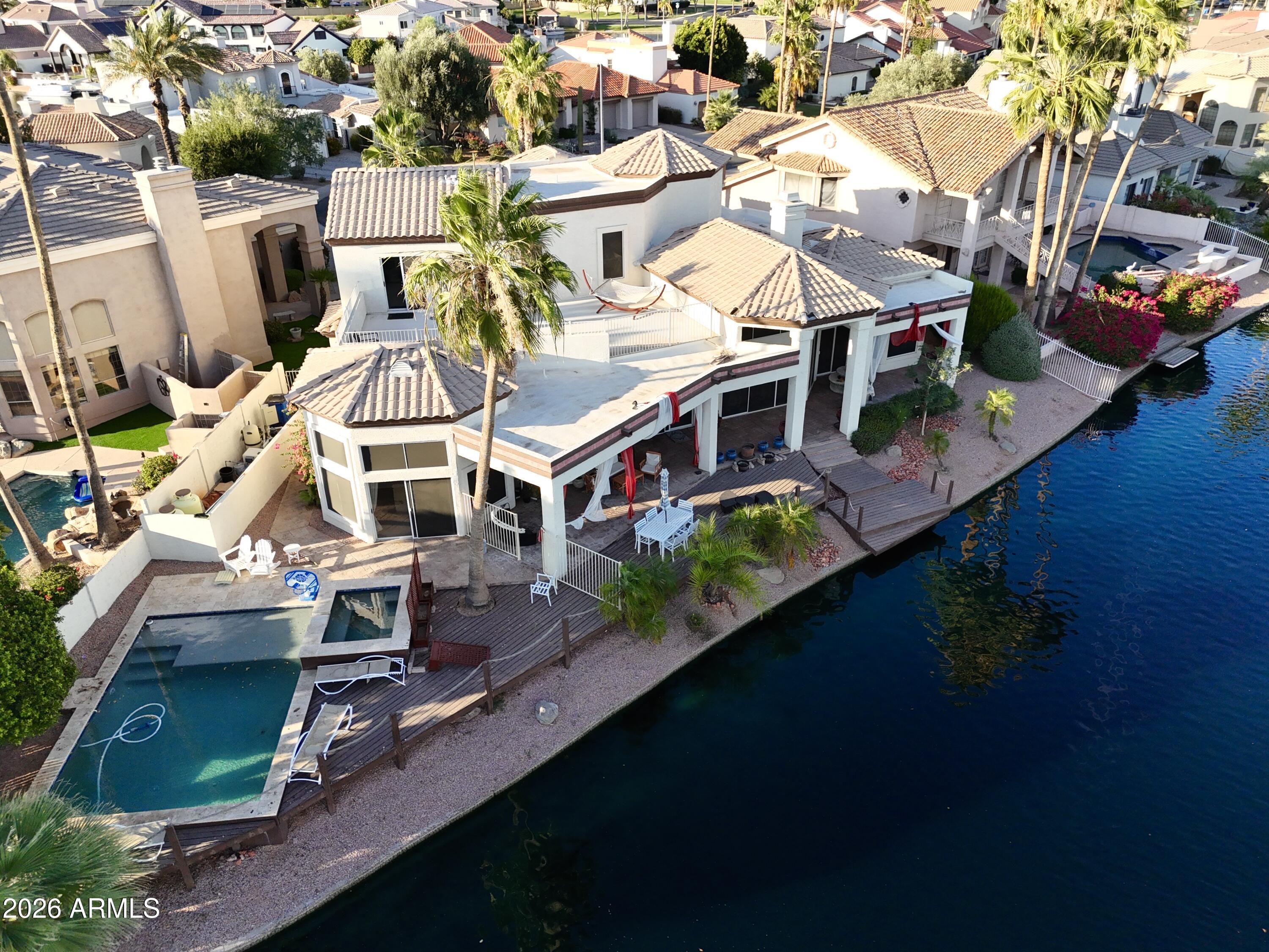 Experience true waterfront living in this exceptional custom home located in the highly desirable lake community of The Islands. Tucked away on a cul-de-sac surrounded by custom residences, this one-of-a-kind property offers breathtaking lake views, a private pool, and an incredible backyard designed for entertaining. Enjoy lakeside dining from the extended balcony overlooking the water, or spend evenings fishing and relaxing from your private boat dock. Inside, the home features a spacious open layout with soaring 20-foot ceilings and expansive waterfront windows that fill the space with natural light. The modern kitchen is designed for both everyday living and entertaining, offering generous counter space, abundant cabinetry, and a seamless flow into the main living areas. The home also includes a formal dining room and separate formal living space, creating the perfect setup for hosting guests or enjoying quiet evenings at home. The downstairs primary suite is a true retreat, featuring two walk-in closets and an oversized spa-like bathroom with plenty of room to relax and unwind. Upgrades can be found throughout the home, making this a rare opportunity to own a truly unique lakefront property in one of the area's most sought-after neighborhoods. Beyond the home itself, the location is hard to beat. Conveniently located in Gilbert with quick access to major freeways, this property is just minutes from both Downtown Gilbert and Downtown Chandler, giving you easy access to some of the area's best dining, shopping, nightlife, and entertainment options while still enjoying the privacy and tranquility of lakefront living. The Islands community is known for its scenic lakes, walking paths, lush mature landscaping, parks, and unique waterfront lifestyle rarely found in Arizona. Residents enjoy a peaceful atmosphere with opportunities for boating, fishing, kayaking, and evening walks around the water, all while being centrally located near everything the Southeast Valley has to offer.