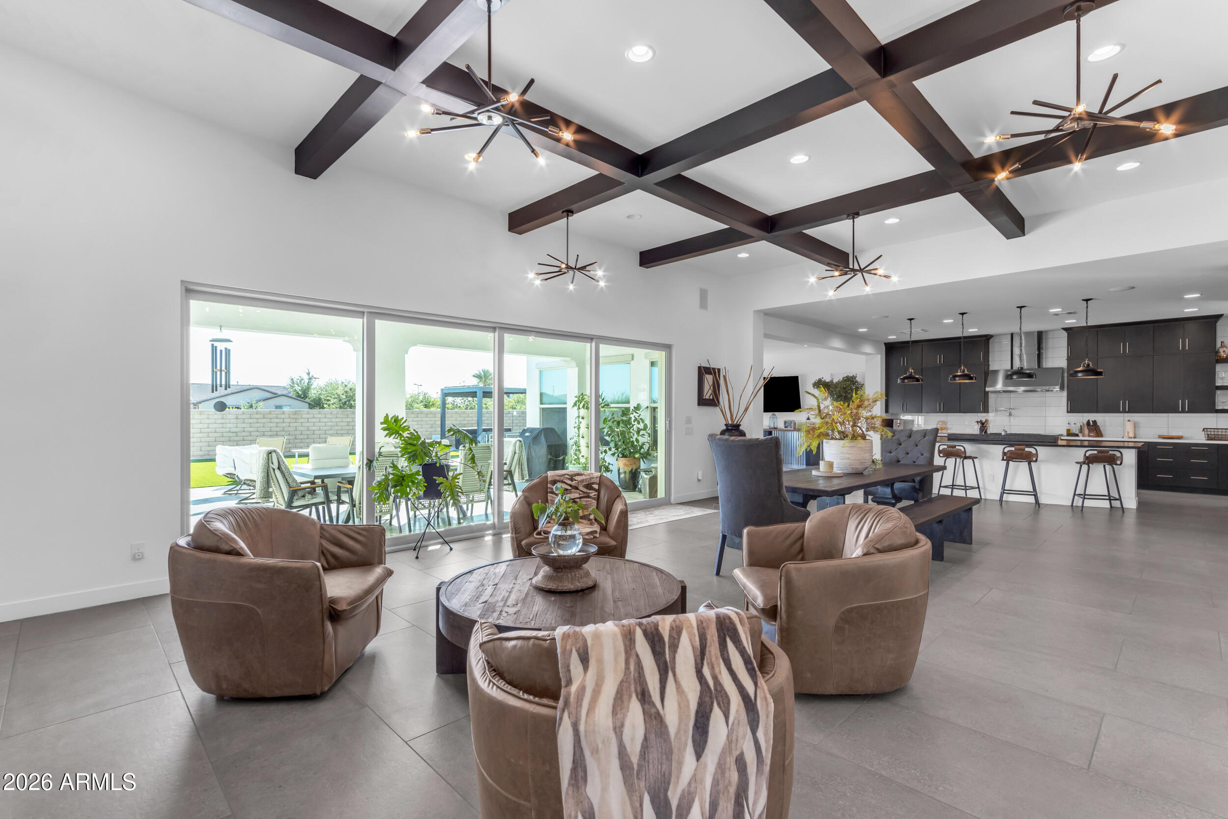 Welcome to an entertainer's dream where architectural intention meets everyday livability. Soaring 12-foot coffered ceilings crown both the great room and formal dining, while a dramatic 20-foot sliding glass wall dissolves the boundary between indoors and out, creating a seamless indoor-outdoor flow designed for gatherings that linger long past sunset. Throughout the home, 10-foot ceilings and curated, design-forward finishes elevate every space. The living area is grounded in large-format concrete-look porcelain tile, creating a sleek, architectural foundation, while thoughtful details like faux wood beam accents layer in warmth and dimension--balancing the home's modern aesthetic. Two expansive living spaces offer the flexibility to host with intention or unwind in a more relaxed setting.

At the heart of the home, a true showpiece: a chef's kitchen that doesn't just function... it performs. Outfitted with stacked cabinetry, soft-close millwork, and a striking leathered granite oversized island, the space is elevated by a full-height glossy backsplash in a clean stacked layout, delivering a polished, modern edge with just the right amount of shine. Premium Monogram Appliances take center stage, including a commanding 48-inch gas range with pot filler, double ovens, and a built-in wine refrigerator--because entertaining should feel effortless, not limiting.
A set of sliding barn doors reveals a private office or den, offering flexibility without sacrificing style.

The primary suite is a retreat in every sense, featuring generous proportions, a spa-inspired bathroom, and an expansive walk-in closet designed for both function and indulgence.

Beyond the main living areas, a thoughtfully designed secondary living wing creates its own private enclave, complete with a separate living room/den that anchors the space. En-suite bedrooms and this living area enjoy private access to a serene courtyard, creating a tucked-away escape ideal for guests or multigenerational living.
Step outside to an oversized lot with no rear neighbors, already prepped with gas and electric for a future pool. For now, unwind in your private spa and cold plunge, or gather around the gas firepit under the Arizona sky--where evenings stretch a little longer and life slows down just enough.
Located within The Estates at Eastmark, residents enjoy access to a private clubhouse complete with a pool, firepits, lounge areas with TVs, a fully equipped workout facility, and a kitchen designed for hosting and connection. Beyond that, the greater Eastmark community unfolds with the Great Parks, featuring a splash pad, play structures, a lake with a riparian stream, event pavilion, open fields, scenic paths and trails, a skate park, and an 18-hole disc golf course.
With highly rated schools for all grade levels, a new 30,000 sq ft library, and close proximity to shopping, dining, Queen Creek Village, Legacy Park, Mesa Gateway Airport, the 202 freeway, and the scenic beauty of Canyon Lake, the lifestyle here is as elevated as the home itself.
This isn't just a home... it's a stage for connection, celebration, and effortless luxury living.