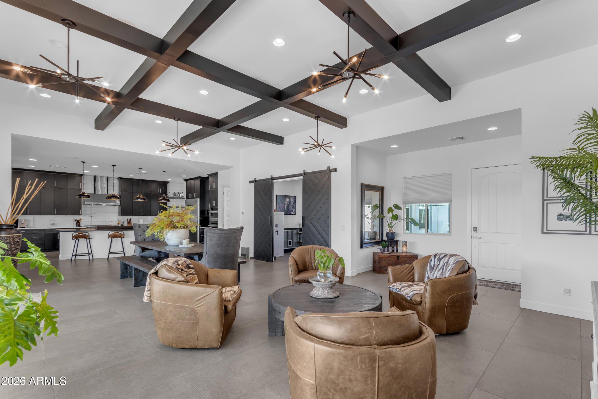 Welcome to an entertainer's dream where architectural intention meets everyday livability. Soaring 12-foot coffered ceilings crown both the great room and formal dining, while a dramatic 20-foot sliding glass wall dissolves the boundary between indoors and out, creating a seamless indoor-outdoor flow designed for gatherings that linger long past sunset. Throughout the home, 10-foot ceilings and curated, design-forward finishes elevate every space. The living area is grounded in large-format concrete-look porcelain tile, creating a sleek, architectural foundation, while thoughtful details like faux wood beam accents layer in warmth and dimension--balancing the home's modern aesthetic. Two expansive living spaces offer the flexibility to host with intention or unwind in a more relaxed setting.

At the heart of the home, a true showpiece: a chef's kitchen that doesn't just function... it performs. Outfitted with stacked cabinetry, soft-close millwork, and a striking leathered granite oversized island, the space is elevated by a full-height glossy backsplash in a clean stacked layout, delivering a polished, modern edge with just the right amount of shine. Premium Monogram Appliances take center stage, including a commanding 48-inch gas range with pot filler, double ovens, and a built-in wine refrigerator--because entertaining should feel effortless, not limiting.
A set of sliding barn doors reveals a private office or den, offering flexibility without sacrificing style.

The primary suite is a retreat in every sense, featuring generous proportions, a spa-inspired bathroom, and an expansive walk-in closet designed for both function and indulgence.

Beyond the main living areas, a thoughtfully designed secondary living wing creates its own private enclave, complete with a separate living room/den that anchors the space. En-suite bedrooms and this living area enjoy private access to a serene courtyard, creating a tucked-away escape ideal for guests or multigenerational living.
Step outside to an oversized lot with no rear neighbors, already prepped with gas and electric for a future pool. For now, unwind in your private spa and cold plunge, or gather around the gas firepit under the Arizona sky--where evenings stretch a little longer and life slows down just enough.
Located within The Estates at Eastmark, residents enjoy access to a private clubhouse complete with a pool, firepits, lounge areas with TVs, a fully equipped workout facility, and a kitchen designed for hosting and connection. Beyond that, the greater Eastmark community unfolds with the Great Parks, featuring a splash pad, play structures, a lake with a riparian stream, event pavilion, open fields, scenic paths and trails, a skate park, and an 18-hole disc golf course.
With highly rated schools for all grade levels, a new 30,000 sq ft library, and close proximity to shopping, dining, Queen Creek Village, Legacy Park, Mesa Gateway Airport, the 202 freeway, and the scenic beauty of Canyon Lake, the lifestyle here is as elevated as the home itself.
This isn't just a home... it's a stage for connection, celebration, and effortless luxury living.