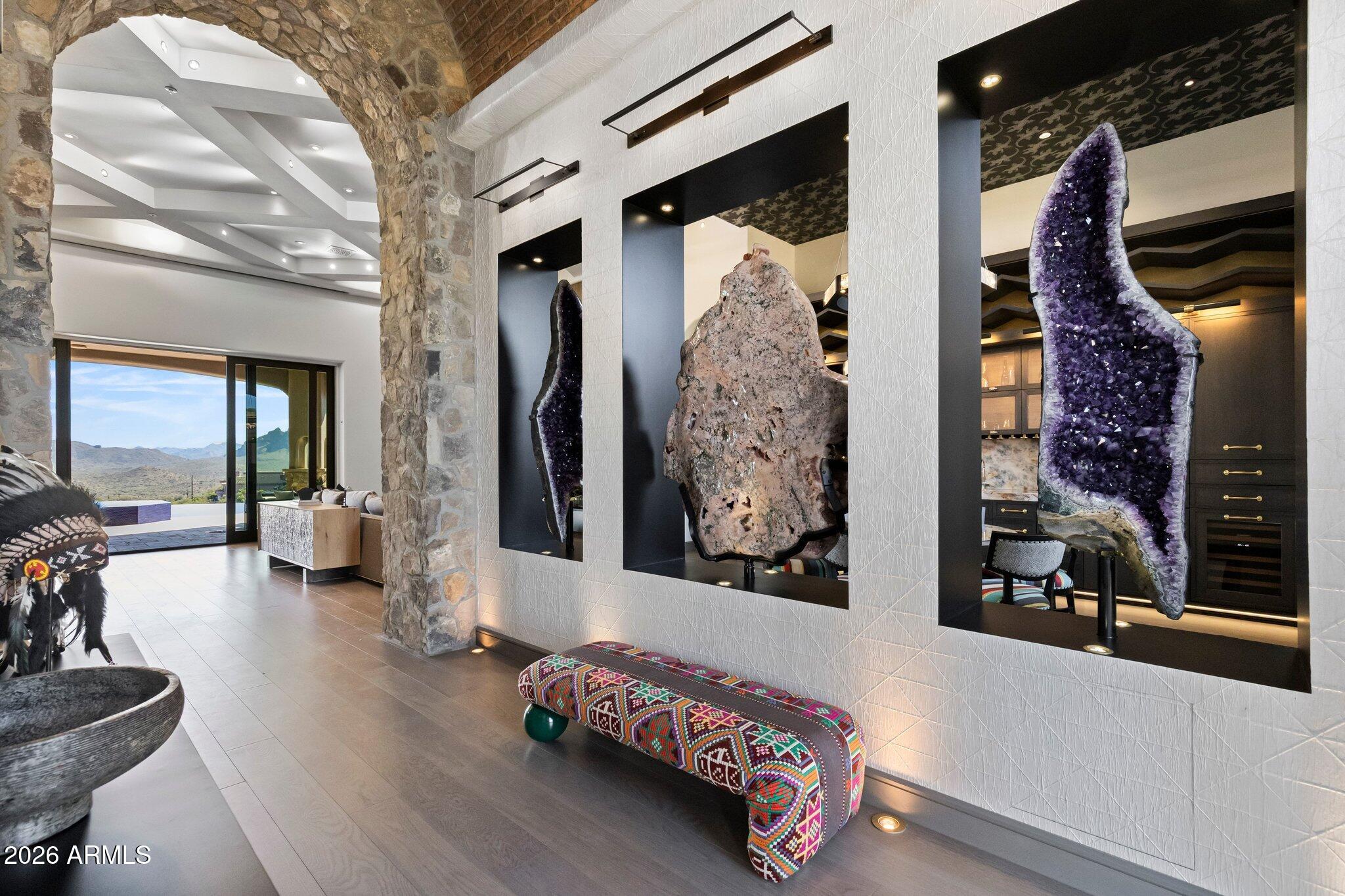 As Seen on AZFamily 3TV|CBS 5 & So Scottsdale June issue, an architectural achievement reimagined by Jaque Bethke on an elevated 1+ acre lot in FireRock Country Club. This 6,007 SF, 5 Bed, 4.5 Ba, museum-quality residence blends raw elemental beauty with world-class technology. Anchored by three 3,000lb motorized amethyst/pink geodes, the home offers seamless single-level living via private elevator. Chef's kitchen features a 12' waterfall island & AI-powered hood. Wellness primary suite boasts Red Mountain views, 4-zone heated floors & steam closet. Fully automated via Josh AI, Control4 & Lutron. The ''Collector's Dream'' garage features 4 over-height, extended-length bays prepped for lifts to accommodate up to 8 cars. Entertainer's backyard with negative-edge pool & spa overlooking Four Peaks and City lights.  This is a curated journey in the Sonoran Desert, designed for effortless living and sophisticated entertaining.  The entire living experience is contained on a single main level. The culinary hub is a masterpiece of form and function, a 48" gas range, custom steel and light AI powered hood, and a high-utility butler's pantry. Adjacent to the casual living areas, the home offers a state-of-the-art home theater with a 10-foot screen, an executive home office, and guest suites featuring private balconies. Residents can enjoy the warmth of a sleek fireplace while taking in unobstructed, sweeping views of Red Mountain, creating a resort-level atmosphere within the home. With Smart Home technology, every element of the home's environment, from lighting and climate to security and media, is integrated for intuitive use.  The "Entertainer's Dream" backyard is designed to showcase Arizona's natural beauty. Expansive travertine patios offer a front-row seat to spectacular sunsets, shimmering city lights, and iconic views of Four Peaks and Red Mountain. With a built-in BBQ and multiple lounging zones, the outdoor space is an extension of the home's elemental luxury, completing this architectural masterpiece.