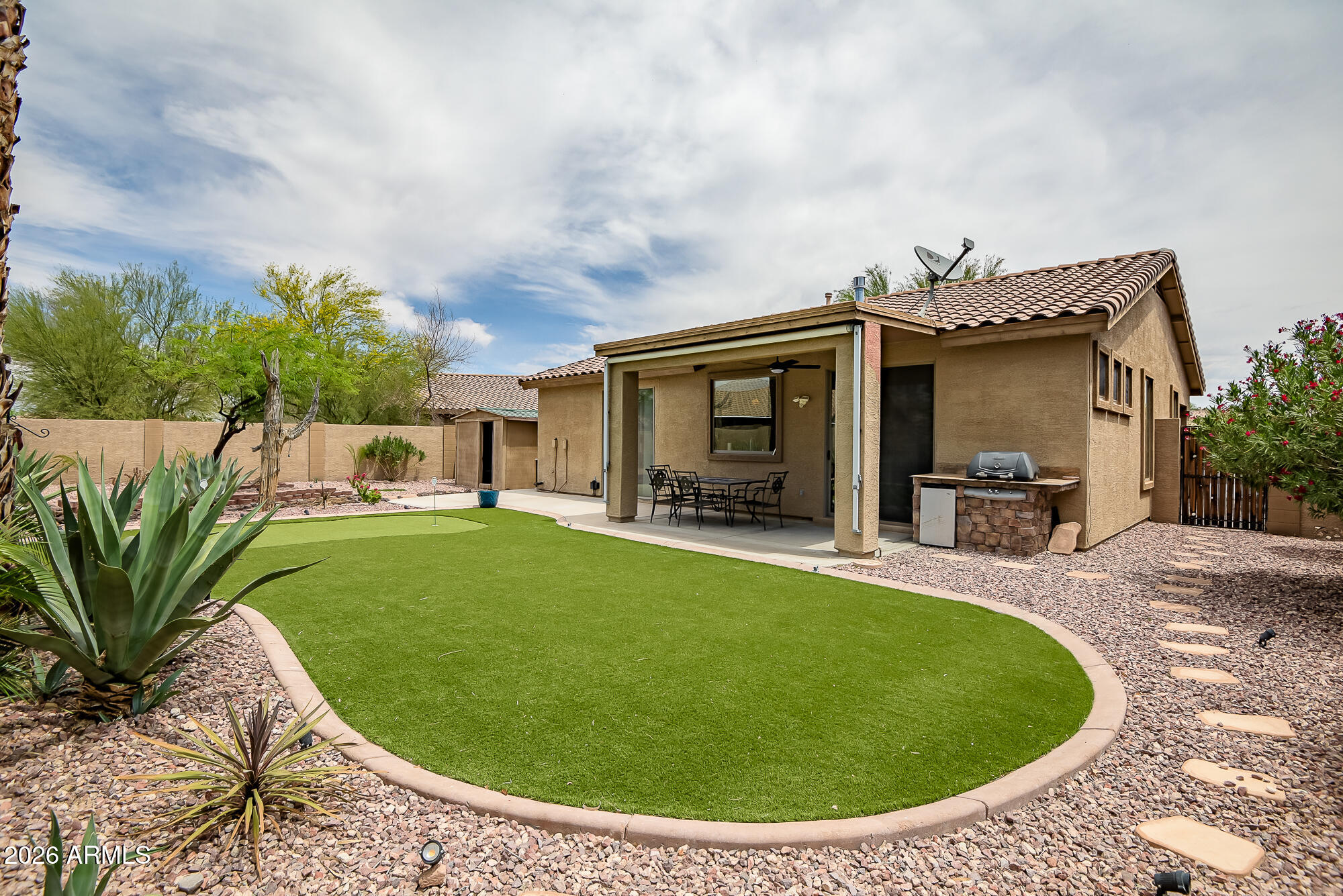 Welcome to this FULLY FURNISHED beautifully upgraded single-story home in highly sought-after Estrella Mountain Ranch! Featuring 2 bedrooms plus a den including Murphy bed, 2 bathrooms, and situated on a spacious lot, this home offers the perfect blend of comfort, style, and Arizona outdoor living plus it may be  sold fully furnished. The backyard is an entertainer's dream with low-maintenance artificial turf, a putting green, cozy fire pit area, and an additional storage shed. Inside, you'll find custom touches throughout including tile flooring, stunning stonework accents, an upgraded fireplace, and a custom bar area in the dining space perfect for entertaining guests. The spacious primary suite features upgraded closet systems and a beautifully remodeled bathroom complete with a large custom tiled walk-in shower. The versatile den offers the perfect space for a home office, workout room, or guest area. This home can also be sold fully furnished, making it an incredible turnkey opportunity for full-time residents, winter visitors, or investors. Located in the award-winning Estrella Mountain Ranch community, residents enjoy access to incredible amenities including resort-style pools, fitness centers, scenic lakes, hiking and biking trails, fishing, and championship golf at the Jack Nicklaus-designed Golf Club of Estrella. The community also offers abundant HOA activities and events including concerts, holiday celebrations, fireworks shows, farmers markets, and more.