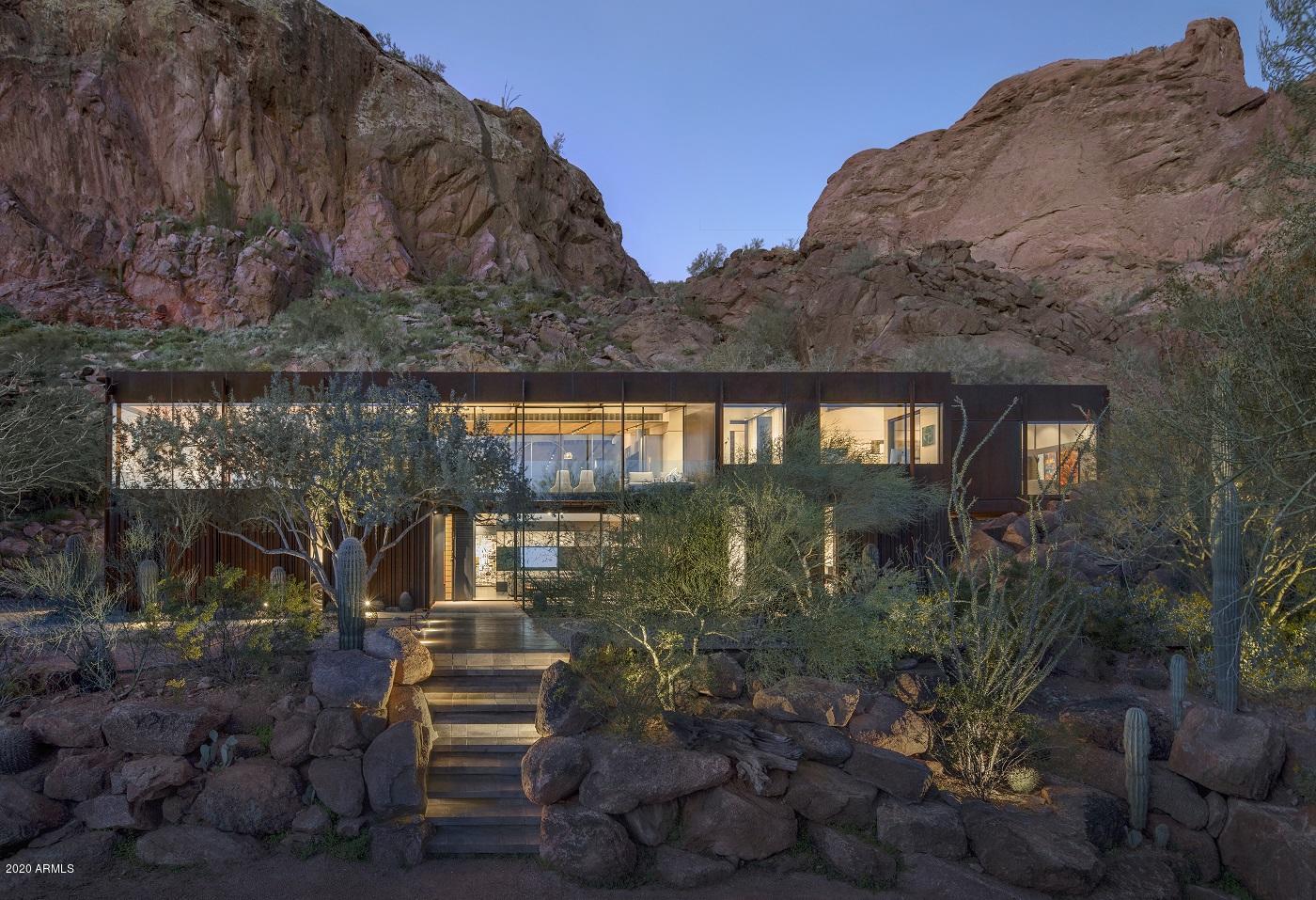 Cliffback, which received the 2020 AIA top honor award for the Western Mountain Region, is nestled into the red rocks of Camelback Mountain, with expansive panes of glass reflecting the landscape and the patina of its steel skin melding into the cliffs that define this
Sonoran desert site. The parti is simple: a cleft in the landscape left behind by an existing scar fits the structure and reveals the pool and upper outdoor living. The house is a shed form rising up to the steep slope of the mountain to the south and capturing the horizon of the northern valley views beyond. The mountain is held back by varying thicknesses of vertical stone clad masonry retaining walls while the building is articulated entirely in hot rolled steel. The exterior of the building is a rhythm of exposed structural columns and custom corrugated cladding mirroring the furrows of the cacti lining the entryway. The steel-clad base of the home
blends with the landscape by day and disappears in the
evening leaving the glass upper level as a glowing piece of the
mountain. The exterior walls fold into the building, leading you
up an oak and steel stair to the living spaces above. The
interior is a study of materials and their connections. Steel
detailing defines the planes of oak, terrazzo, plaster, and
stone finishes. Much like the structure and its relationship to
its site, it is the crafting of the intersection and connection of
these materials that define this architecture. Each space
takes advantage of its mountain views. Custom outboard
steel and glass sliding walls open to bring the rock
outcroppings into the experience. The house becomes one
with its landscape leaving only the question of time. It is as if
it was always there, connected and part of its mountain site.