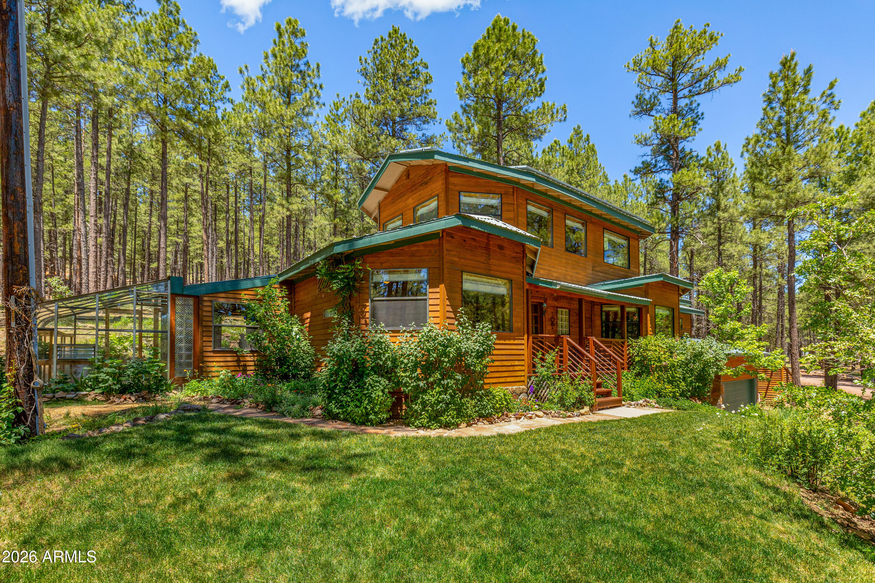 Tucked into the ponderosa pines on Hidden Hollow Road en route to Arizona Snowbowl, this custom-built 3-bedroom, 1.5-bath cedar cabin blends craftsmanship with forest living. Step outside to two patios, a hot tub, professional landscaping with sandstone steps and walkways, a landscaped pond, and a yoga platform set among the trees. A wildlife corridor draws deer, elk, birds, and more. Inside, solid wood, custom alder cabinets, Bruce oak floors, and Doug fir beams meet large windows full of forest views. The upstairs loft delivers a 180-degree vista, complemented by a cedar sunroom and attached greenhouse, both with flagstone floors. A large on-grid solar system supplies electricity much of the year, and a fan-assisted fireplace adds warmth. Firewise certified. A true cabin in the woods.