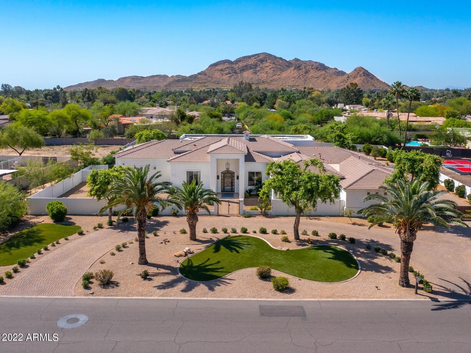 Exquisite Views of Mummy Mountain, Custom home boasts soaring 24 foot ceilings, 8 foot doors throughout with an open flowing floor plan. 5,200+ square feet with 5 en-suite bedrooms and 5.5 bathrooms, a huge chefs kitchen with stainless steel appliances, gas cook top, home theater, spacious great room complete the open concept .  The resort back yard of your dreams. Full size sport court, new putting green.  Low Maintenance artificial Turf plus a large Built in BBQ and grill station. Sought after North/South exposure lights up Mummy Mountain for cocktails by the pool, private gated driveway and the sliding wall of glass to the patio compliment the outdoor experience. Owned solar completes this luxury compound