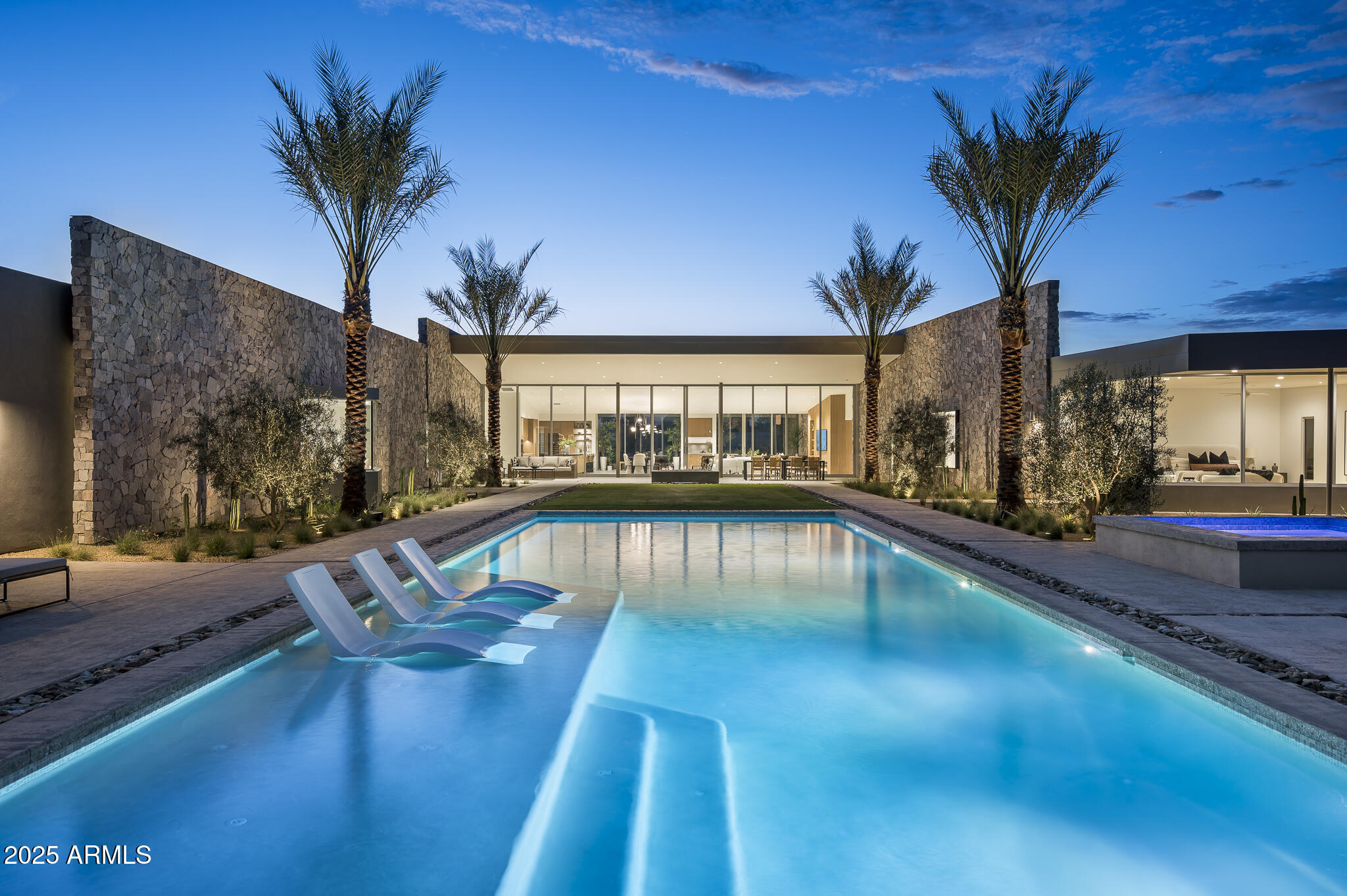 Welcome to the newest masterpiece brought to you by Vasbinder Development and The Irvine Asset Group. The recently completed Casa Blanca north residence is a union of design and material, set against the backdrop of an iconic Arizona landmark, Camelback Mountain. This stunning desert contemporary home is comprised of two stone clad wings, flanking a great room of panoramic glass between, the arrangement perfectly framing dramatic mountain vistas. Upon arrival, the front entry walk opens to a generous front garden under a lattice of light and shadow. Stone and sunlight extend into the home, blurring the sense of inside/outside, a common theme throughout. The great room is the heart of the home, under a floating butterfly wing roof, paired with large format porcelain floor, bringing an organic warmth to the space, while seamlessly connecting to the stunning gourmet kitchen. The home features five bedrooms including a private primary suite with unobstructed mountain views, a large guest suite, three en-suite bedrooms, dedicated office, rec/theater room and flex room for a gym or whatever the new homeowners would like. Home automation controlled by Control4 which allows the homeowner full control of all systems inside and outside of the home with limitless options to customized.  Plans for a beautifully designed 845-square-foot guest casita have already been approved and will transfer with the sale, offering a rare opportunity to further elevate and expand this already extraordinary property.
The homes 7,781 square feet was designed by Worksbureau alongside Tact Design Studio boasts over 3,000 square feet of covered patio space with the ability to open the large 14' operable multi slide door system truly letting the outdoors in. Berghoff Design Group artfully crafted and installed an exterior landscape design that rivals many local resorts, with lush surroundings, an expansive 60' lap pool, heated spa, two firepit sitting areas, and room for a pickleball/sport court/putting green, providing the homeowner with the perfect setting for entertainment and family living. This stunning contemporary home in the heart of Paradise Valley is ready to welcome its new owners. With meticulous attention to detail and a sleek design, this property offers the perfect blend of luxury, comfort, and modern living. Don't miss your chance to own a piece of paradise in one of Arizona's most coveted locations.