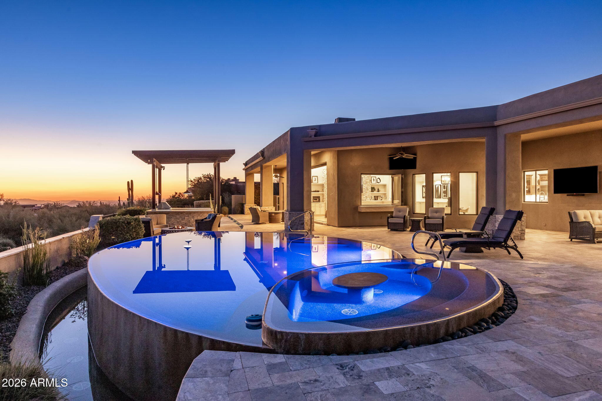 Positioned on a private cul-de-sac within the gated community of Boulder Crest at North Troon, this exceptional 5,147 sq ft, single-level residence delivers the ideal blend of indoor-outdoor living and breathtaking desert surroundings. Designed for both elevated entertaining and effortless everyday living, the home captures north/south exposure, dramatic sunsets, and city-light views to the west, all framed by the natural beauty of the Sonoran Desert.
At the heart of the home is the grand great room with soaring ceilings and expansive multi-slide glass doors creating a seamless connection between interior and exterior spaces. A striking floor to ceiling custom gas fireplace anchors the room beneath an 85-inch television, complemented by surround sound, making it an ideal setting for hosting, relaxing, or enjoying cinematic evenings at home.
The adjacent full bar elevates the entertaining experience, featuring retractable windows opening directly to the backyard, perfect for indoor-outdoor gatherings.  Thoughtfully designed for functionality and flow, the kitchen connects naturally to both the great room and the separate formal dining room, allowing for intimate dinners or larger celebrations.
The outdoor living spaces are a true extension of the home. A pergola-covered stone outdoor kitchen is perfectly situated, overlooking a stunning raised perimeter overflow pool. Multiple seating and conversation areas invite relaxation, entertaining and sunset viewing, while the surrounding natural open spaces (NAOS) enhance privacy and preserve the serene desert atmosphere.
The primary suite and additional living spaces are thoughtfully arranged on one level, emphasizing comfort, accessibility, and privacy. High ceilings throughout the home enhance the sense of volume and light, while carefully placed windows and multi-slide doors frame the desert landscape.
Located in one of North Scottsdale's most coveted enclaves, Boulder Crest offers a rare combination of exclusivity and access. Residents enjoy proximity to Troon North Golf Club, nearby tennis courts, and the extensive walking and biking paths of Browns Ranch Recreational Area, placing world-class outdoor recreation just moments away.
This residence is a refined desert retreat offering privacy, comfort, and connection to nature. A rare opportunity to own an exceptional property in one of North Troon's premier gated communities.