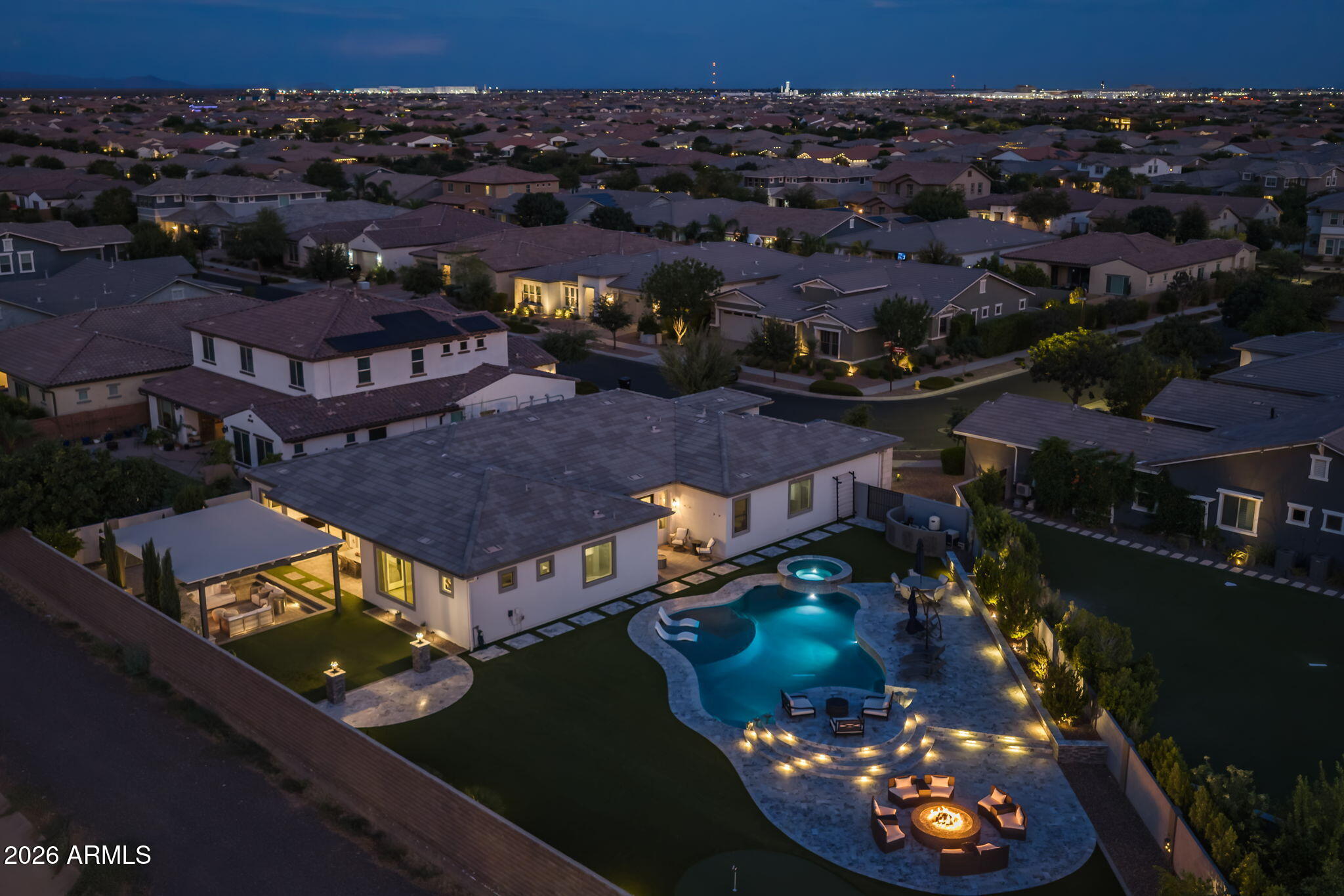 Sitting on over 16,000 square feet in the heart of Eastmark, this is the lot size you simply do not find in this community, and the home built on it does not disappoint. From the moment you arrive, the scale and curb appeal make an impression before you ever step inside. Step through the front door and the interior delivers immediately. Modern square corners, coffered ceilings, and crown molding in the living room and primary suite give the home a custom, architectural feel that is rare. The 12-foot full wall slider connects the main living area to the backyard and floods the space with natural light, while the electric fireplace anchored by a stone accent wall makes the living room a genuine gathering place. Open to the kitchen, this space flows exactly the way a home at this level should. The kitchen is the heart of this home, and it is absolutely massive. A breakfast kitchen extension with its own sink expands the footprint even further and leads directly into the formal dining room, creating a natural flow from cooking to entertaining. Cabinetry runs floor to ceiling, with the top row finished in glass with interior lighting for a designer touch. The two-tone quartz counters are a showstopper in their own right, with a distinct island surface that sets it apart from the perimeter. A farmhouse sink, under-cabinet lighting, and an island wrap make this kitchen both beautiful and genuinely functional. Two custom glass barn doors bring both form and function to the layout, one defining the flex room or studio space, the other separating the front hall from the formal dining area. The formal dining room opens directly to the backyard through French doors, and the primary bedroom offers its own private French door exit to the exterior. Five-and-a-half inch baseboards, wood plank tile throughout the main living areas and primary bedroom, and carpet in two secondary bedrooms complete the interior picture. The primary bath is a true retreat, featuring a freestanding soaking tub, a super shower with rainfall showerhead, and floor-to-ceiling tile work. The laundry room includes cabinets and a sink, and the garage is outfitted with storage racks and a mini split unit for year-round comfort. Step outside and the backyard delivers on every level. A massive pool anchors the space, complete with a large baja step, a raised hot tub with overflow into the pool, and Turkish marble surround with multilevel seating areas. A sunken seating area sits beneath a pergola, centered around a large gas fireplace, with a circle gas fire pit nearby for cooler evenings. Artificial turf, a putting green, a gas stub for the BBQ, two side gates, and gutters around the full perimeter of the home complete a backyard that is as functional as it is impressive. Located in the gated and highly sought-after Estates at Eastmark, residents enjoy access to resort-style amenities including a community pool, fitness center, spa, parks, pickleball, and a full calendar of events and activities that make this one of the most connected communities in the East Valley. With custom finishes, a backyard built for Arizona living, and a lot size that almost does not exist in this zip code, this one is not easy to walk away from.