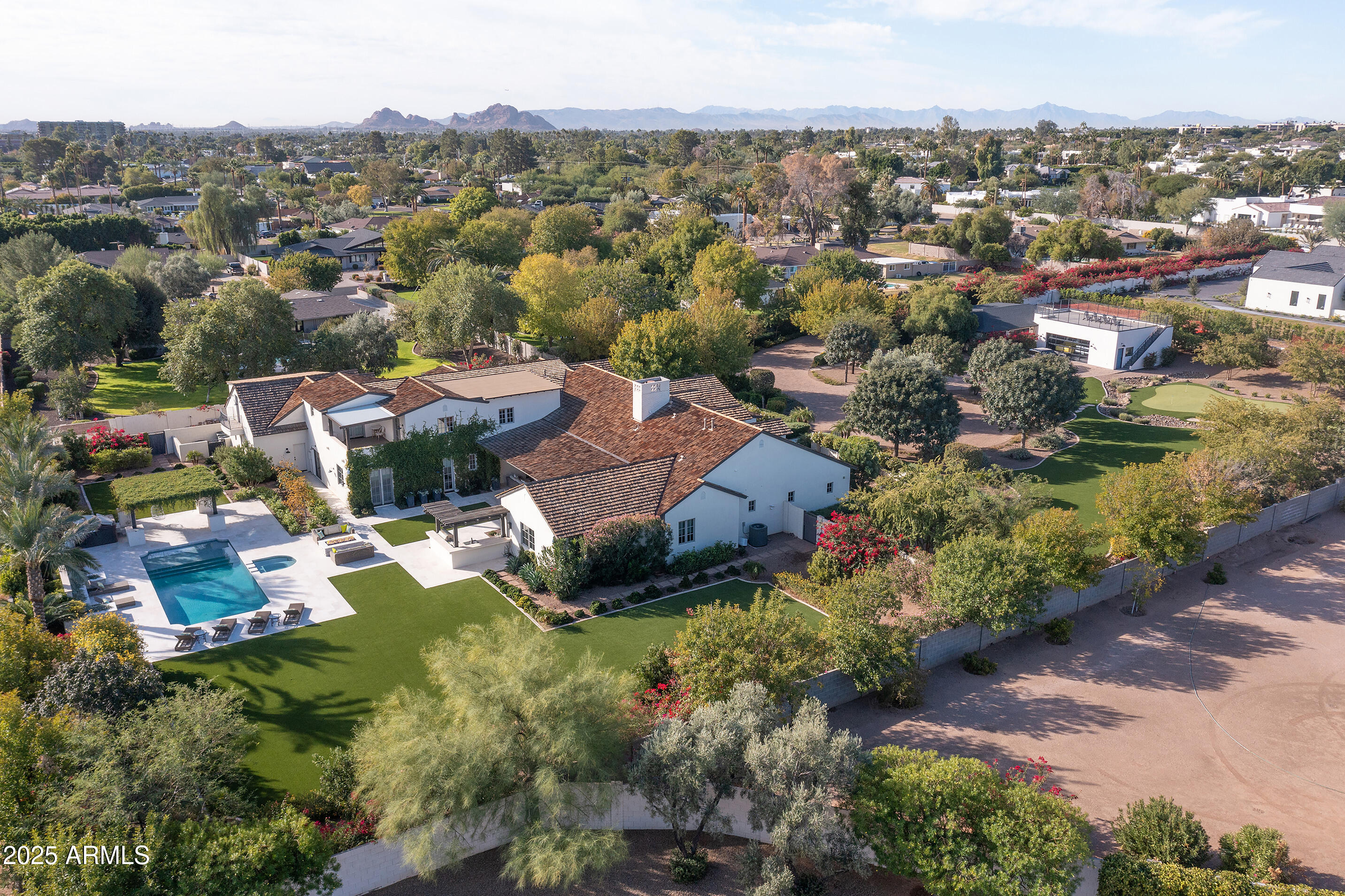 Situated on nearly 2 ACRES(1.962) thru a 300 FT BOUGAINVILLEA-LINED DRIVE this private oasis boasts huge grounds + Camelback Mtn views. The property has $750,000 of new landscaping with 14,000 sq ft of pet friendly turf w/cooling system, 5 hole chip+putt + new pool +spa near an ivy-draped pergola. Beautiful white washed brick walls, light oak floors, and high ceilings w/ wood beams give a romantic farmhouse vibe. Built in 2011 w/a major renovation in 2018, a stunning entry opens to the great rm, gourmet kitchen + diningrm. The main living areas including the primary bedrm plus 2 bedrms, an office+den are on the main level w/ no steps. Two more bedrms are upstairs. PERFECT FOR A CAR COLLECTOR, there are 9 garages- a separate 4-5 GARAGE BUILDING  w/ connected office + 5 garages at the home. There is 80 ft of outdoor space for an RV. More photos of separate garage coming.