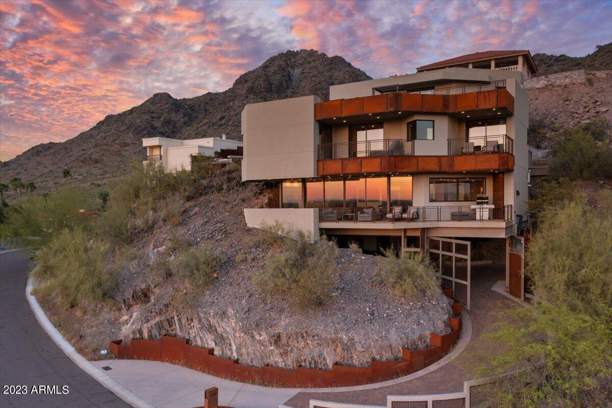 Experience the ultimate desert living at its finest in this exquisite modern architectural masterpiece nestled at the edge of Piestewa Peak Mountain. The 'House Inside a Rock 'has been thoughtfully crafted to appear as if it grew out of the surrounding terrain, seamlessly blending with the natural beauty of the desert landscape.The careful placement of the home, nestled into the rocky terrain, creates a sense of harmony and balance, as if the home was always meant to be there. The use of steel, concrete, and glass in the construction of the home adds a modern and sophisticated element to the rugged natural surroundings, creating a stunning contrast that is both striking and harmonious. From the moment you arrive, a hand-installed paved curve driveway surrounded by the raw beauty of the desert rock welcomes you. With space for up to 4 luxury vehicles , privacy and security is paramount, setting the tone for the awe-inspiring grandeur of this property.This motor court, enclosed by custom steel open paneling and surrounded by the rugged mountain walls, provides a spacious and secure environment for you to park and admire your vehicles. 

As you ascend to the main living spaces, you'll be transported to a world of unparalleled luxury and craftsmanship. The journey to the top is made even more special by the Otis commercial elevator, which envelopes you with its quilted steel panels and feels like a work of art in its own right or take the steel stairs and admire the natural rock mountain wall before arriving at the gallery pivot door stunningly created of steel and glass. Step inside to discover the 180-degree city and sunset views that take center stage, but it's the linear wall of fire and glass against the back-lit raw mountain side that steals the show. This mesmerizing display is a true testament to the creativity and skill of the artist who brought this stunning vision to life.
The main living space is a perfect blend of art and function. 
The oversized professional kitchen is appointed with beyond-luxury appliances, including a Wolf six-burner and grill gas cooktop, Thermador side-by-side refrigerator, double ovens, and two dishwashers. The walnut cabinetry, quartz and iron counters, and automatic sliding window all work together to create a truly remarkable space that is as beautiful as it is functional.
The great room boasts an unparalleled indoor-outdoor living experience with its floor-to-ceiling automated glass panel doors. As you slide the panels open, the lines between the interior and exterior blur, allowing for an unobstructed view of the breathtaking cityscape and sunset vistas.
The second floor is dedicated to the owner's suite and two private ensuites, each with its own private balcony and perfectly placed windows to optimize the incredible views. A fourth room, currently used for laundry and hobbies, completes the floor. 

The owner's suite is a true sanctuary, complete with a sitting room, balcony, floating walnut cabinetry, soaking tub, generous shower, vessel sinks, and expertly designed closet showcases walnut cabinetry.providing ample storage for your prized possessions. To further enhance your daily routine, a conveniently located washer and dryer can also be found in this space. With its thoughtful design and luxurious amenities, this closet is the perfect retreat for any fashion enthusiast.
Just half a level up from the second floor suites, a walkway leads you to a pool terrace nestled within the natural rock formations of the mountain. The terrace is surrounded by steel walls and desert planters, offering a sense of privacy and tranquility. From this vantage point, you can soak up the stunning views of the desert landscape and the twinkling city lights. The heated pebble tech, negative edge pool and spa provide the perfect place to relax and unwind all year long, all while enjoying the convenience of an automated system that requires no manual upkeep.
The top level is currently shown as an entertainer's dream, including a wet bar and full bathroom,  Here, you can exit onto the "sky yard," an enormous open-air rooftop desert garden, as edgy as anything you would find in the top cities of the world , complete with hardscape, turf, trees, fire feature, and space to entertain all your friends, this is the ultimate in desert living.
Every inch of this 4 level house is a true testament to the beauty and power of modern design, it has been crafted with the utmost attention to detail and a true appreciation for seamlessly blending to its natural surroundings. With breathtaking views, unparalleled craftsmanship, and an ideal location, this is an opportunity not to be missed. This home is a truly a "work of art".